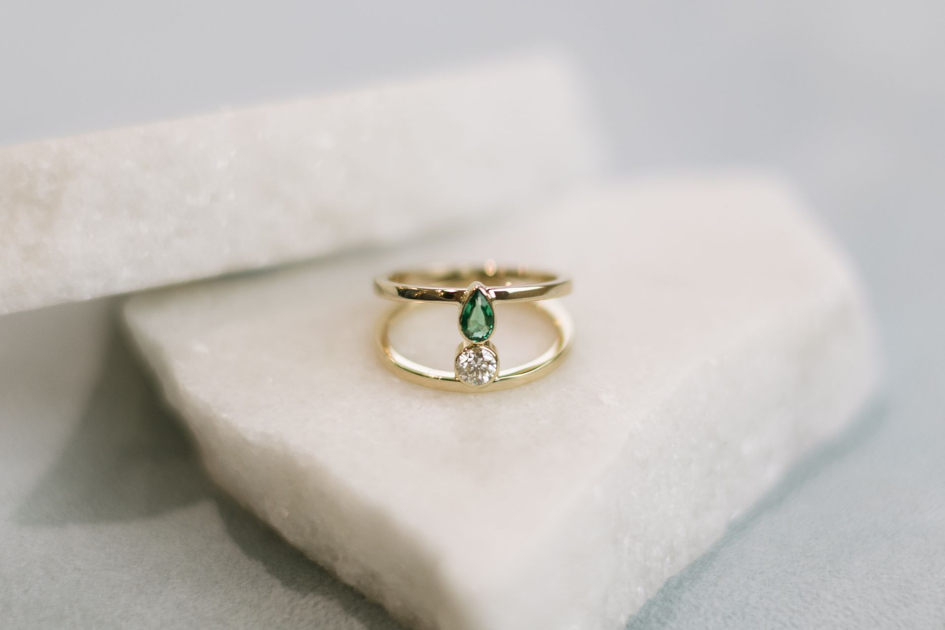 Gold ring with a green gemstone and a diamond on a white marble surface.