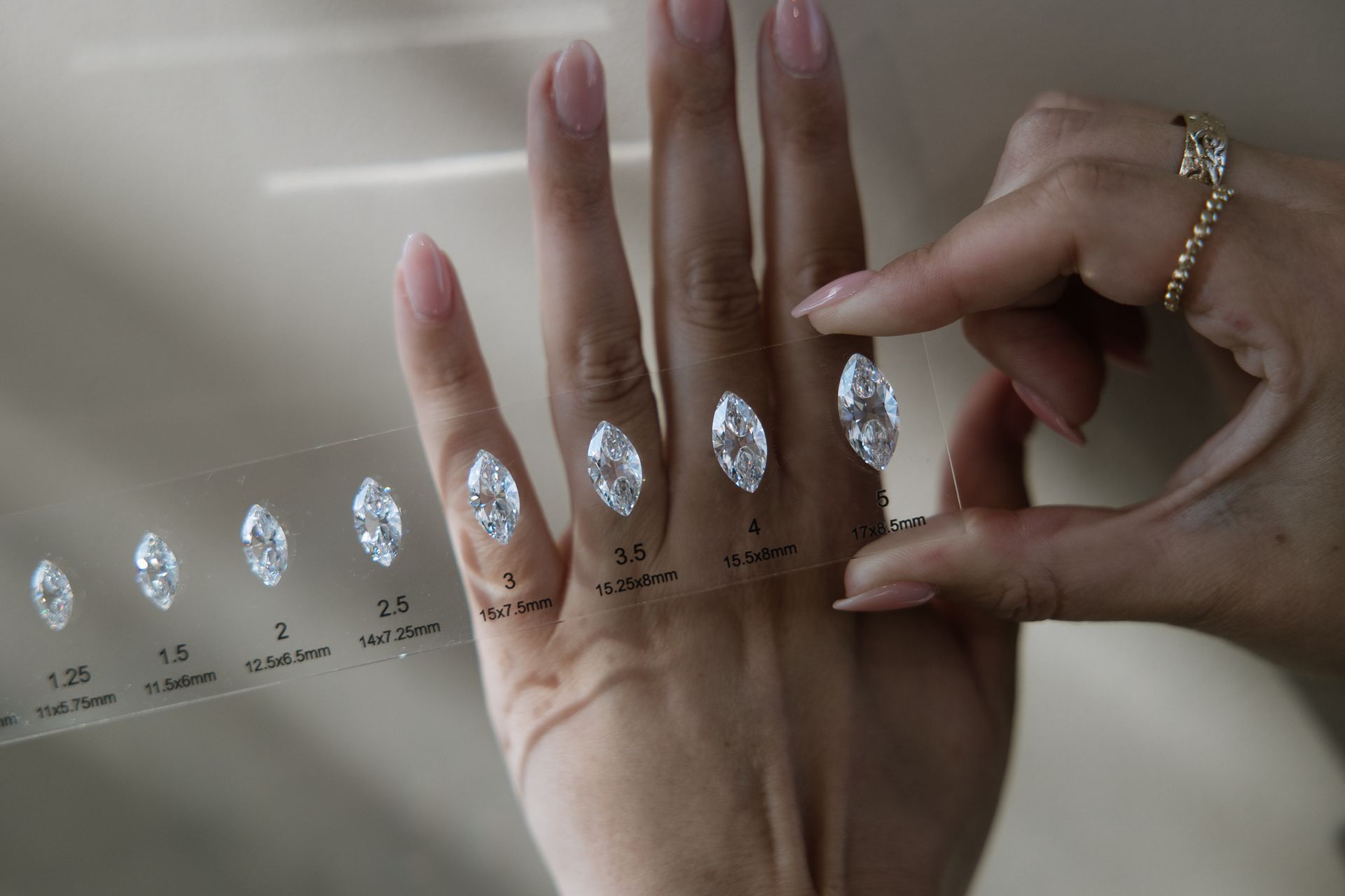 Person comparing marquise-cut diamond sizes on a hand using a size guide.