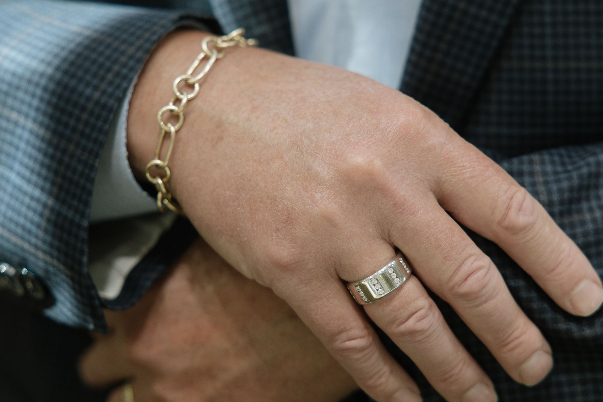 Man's hand with gold ring and bracelet, resting on jacket.