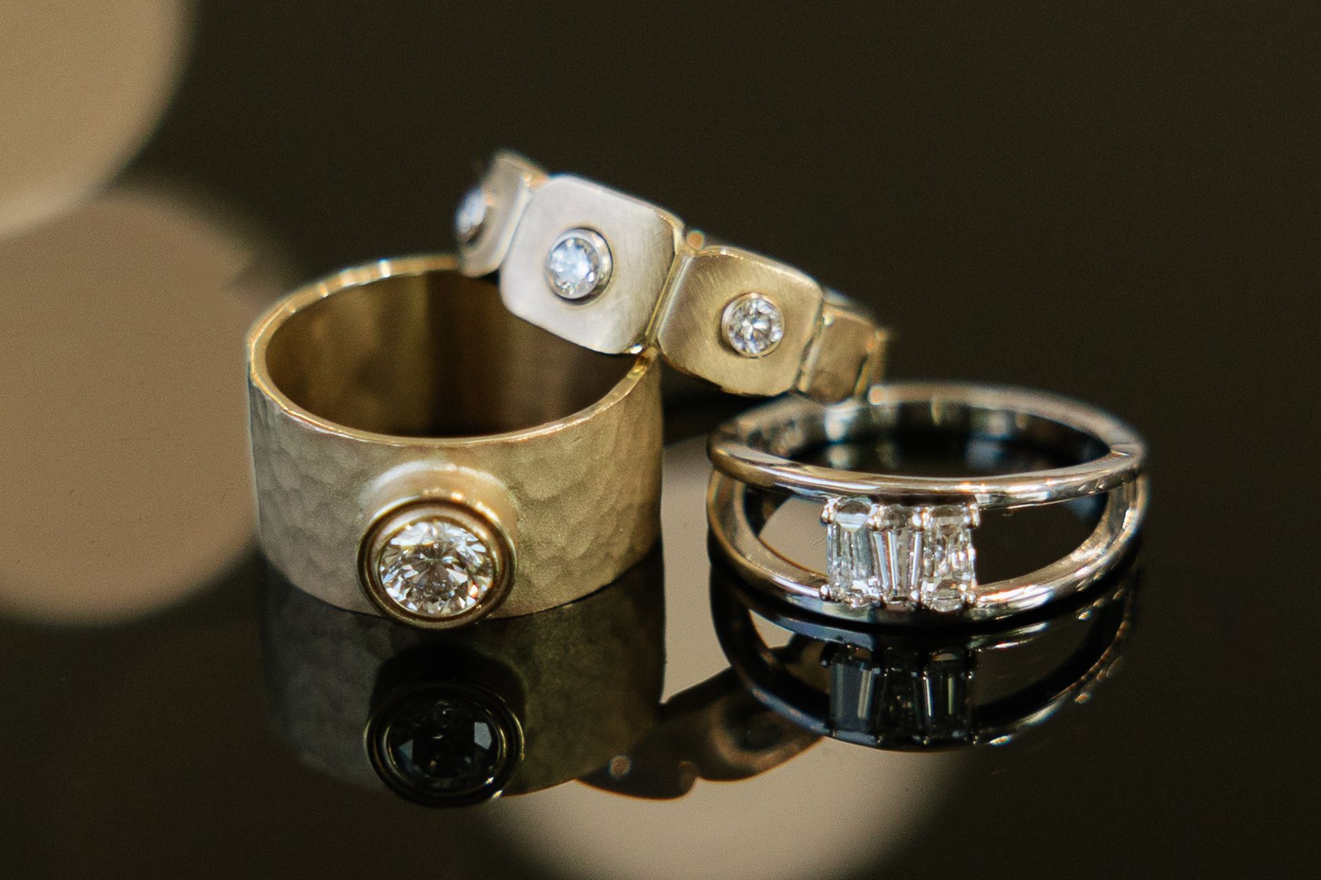 Three gold and silver diamond rings on a black reflective surface.