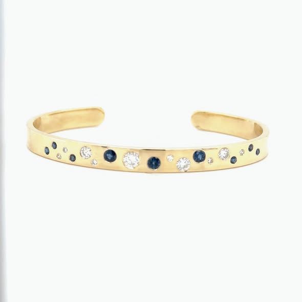 Gold cuff bracelet with scattered blue sapphires and diamonds.