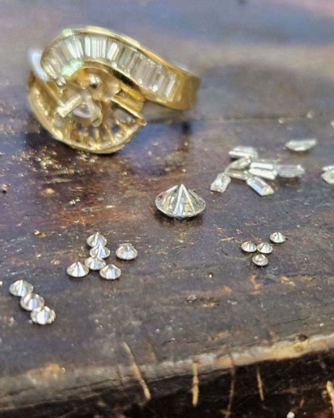 Gold ring with diamonds next to loose diamonds on a wooden surface.
