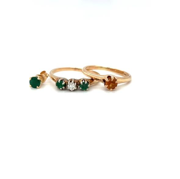 Three gold rings, one with a single orange gemstone, another with three green gemstones, and an earring with a green gemstone.