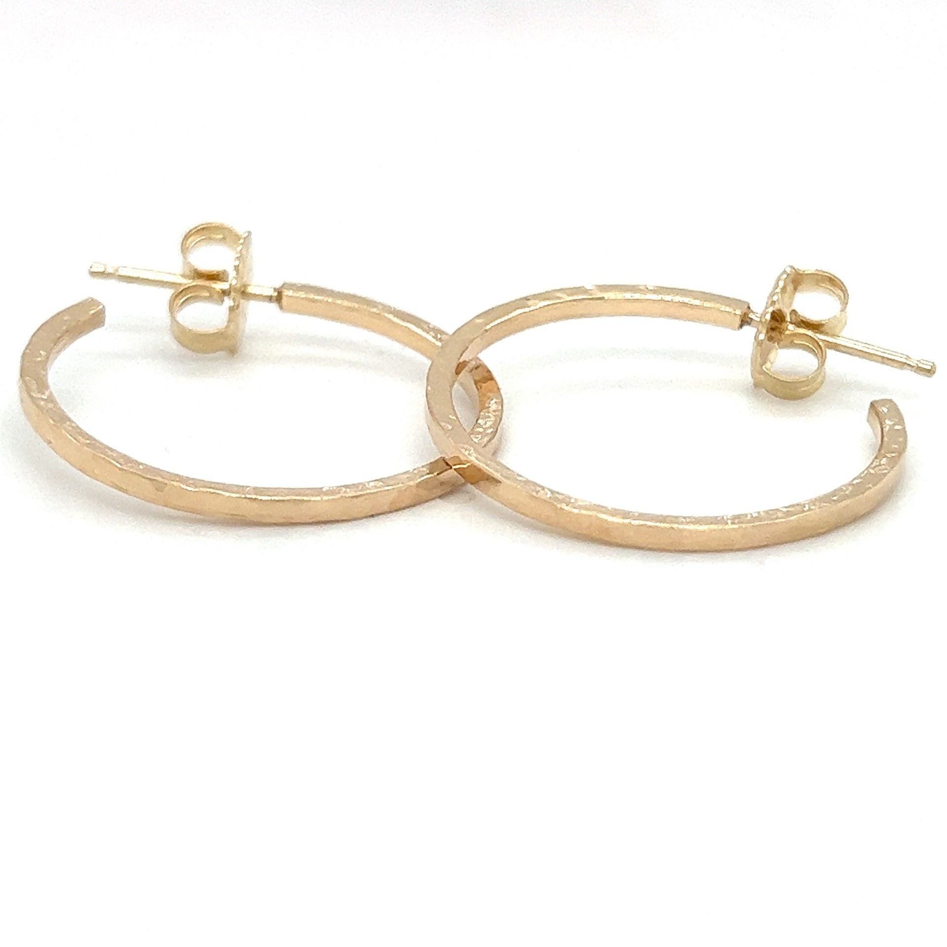 Gold-colored hoop earrings with textured outer edges, laying on a white surface.
