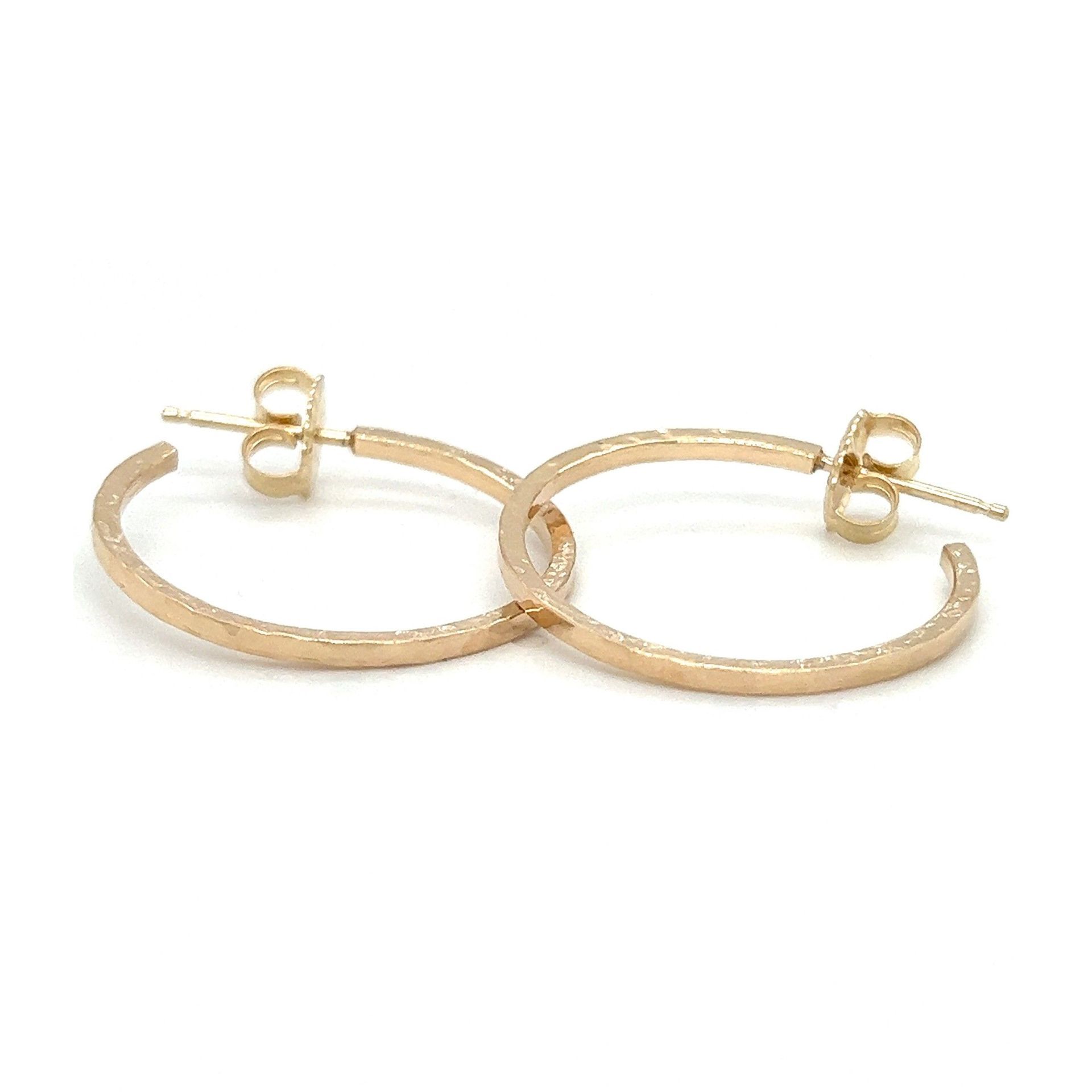 Gold-colored hoop earrings with textured outer edges, laying on a white surface.