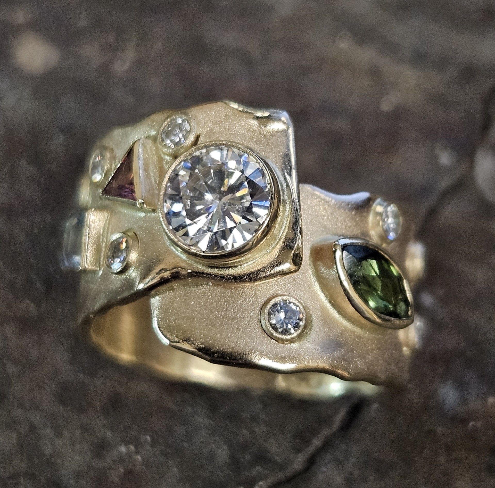 Gold ring with a large central diamond and various smaller gemstones embedded.