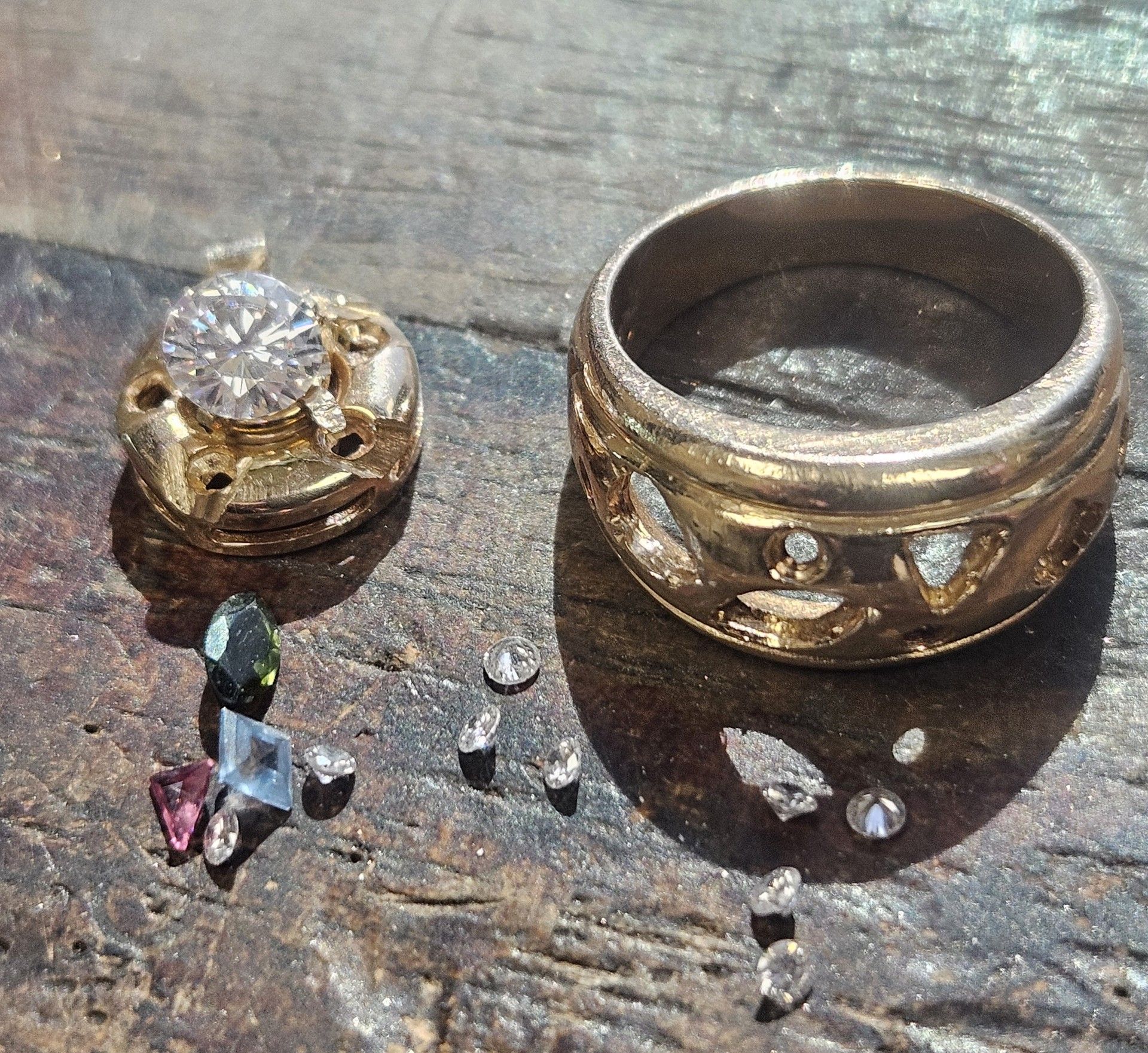 Gold rings and loose gems on a wooden surface, suggesting repair or jewelry work.