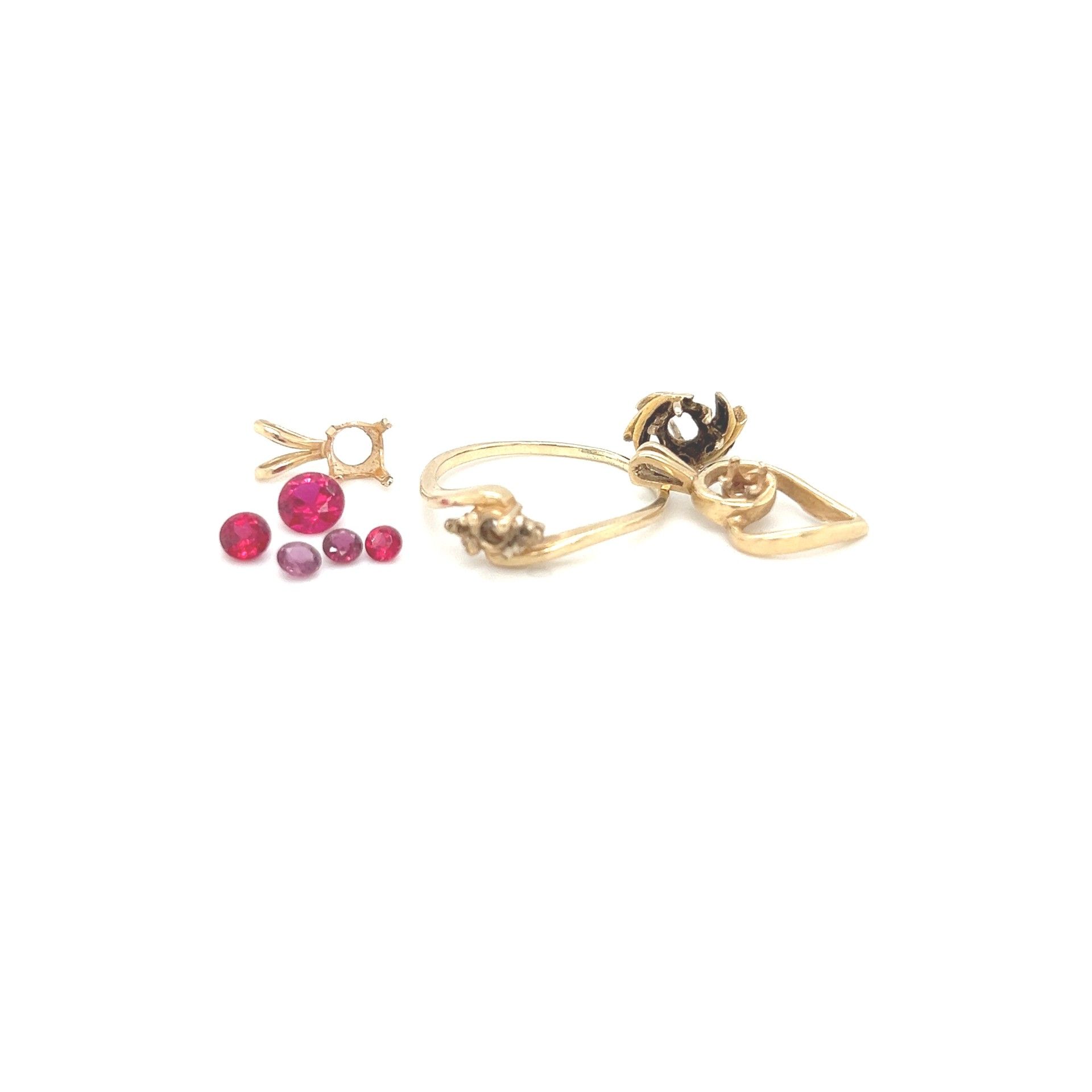 Gold rings and loose red gemstones on a white surface.
