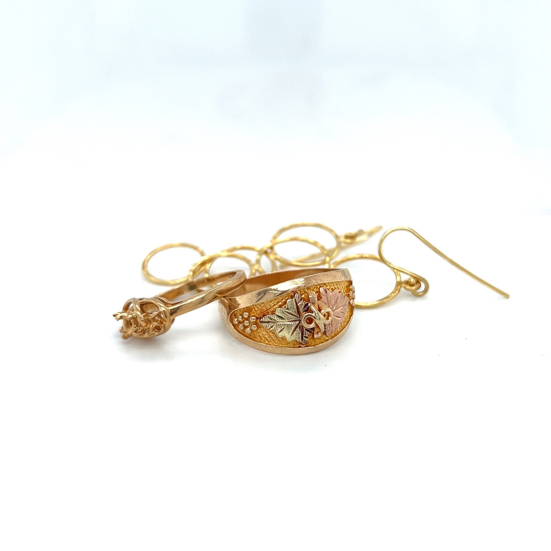 Gold jewelry on a white surface, including a diamond ring, floral ring, and chain.