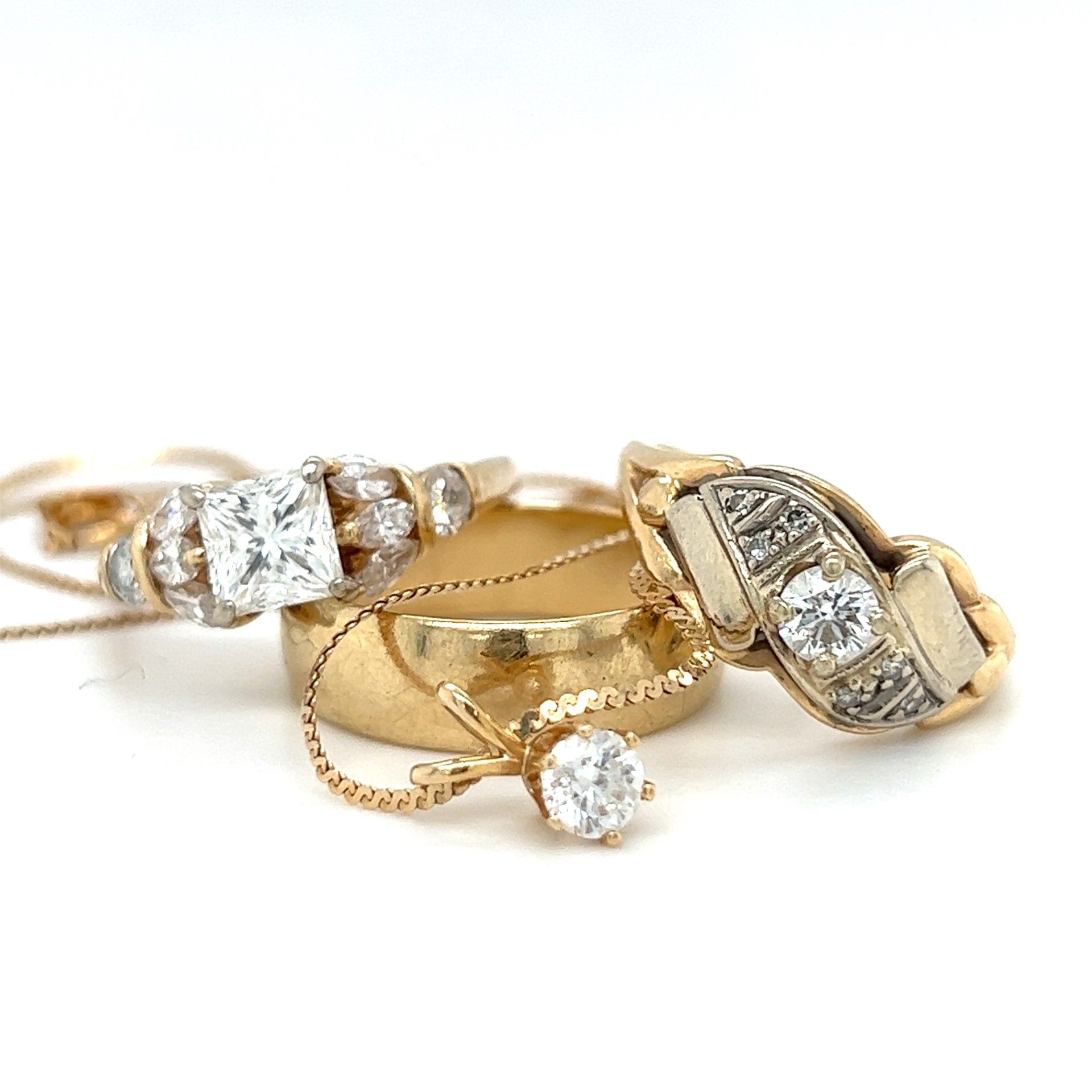 Close-up of gold jewelry on white: diamond engagement ring, wedding band, and pendant necklace.