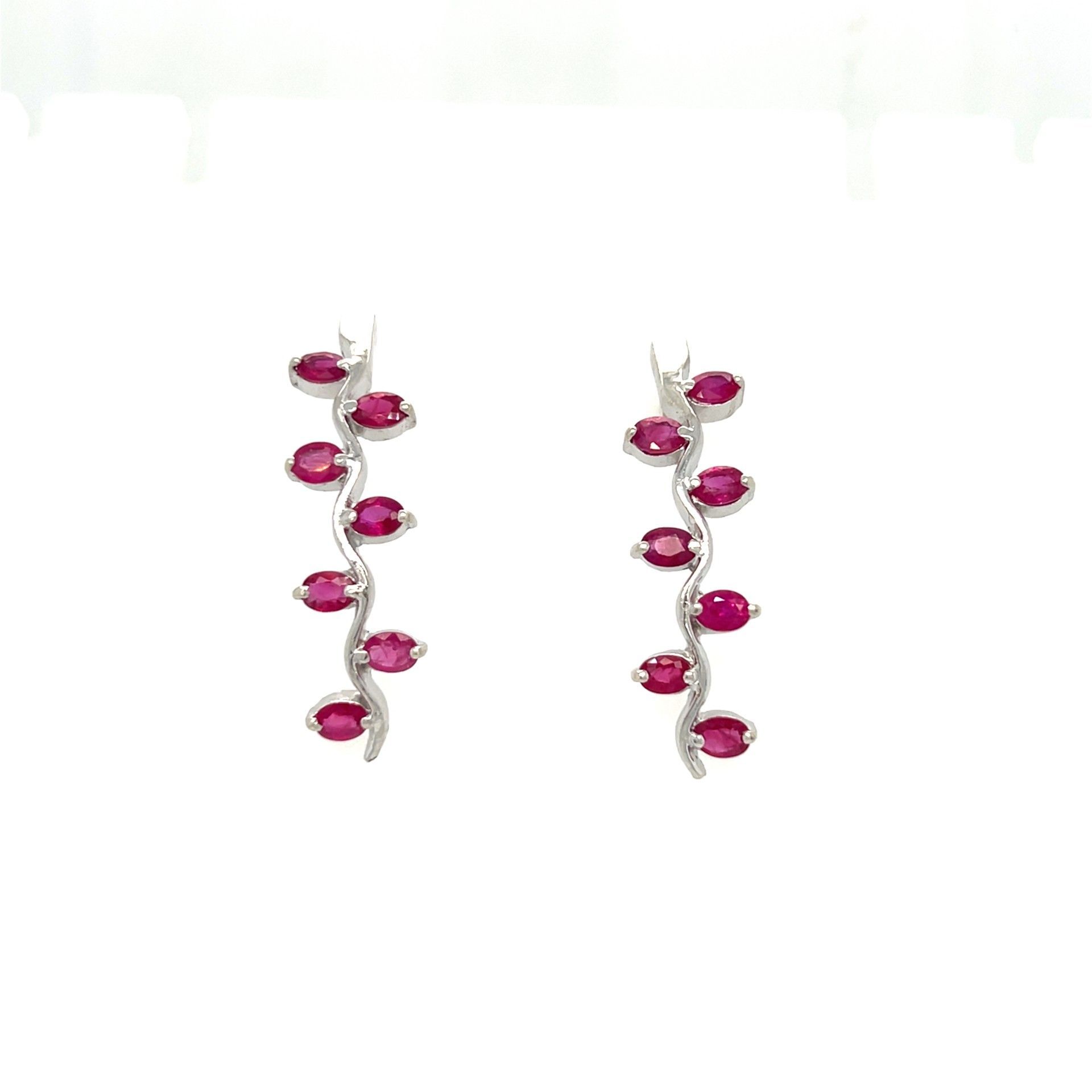 Pair of ruby and diamond earrings on white background. Ruby gemstones form a vine shape.