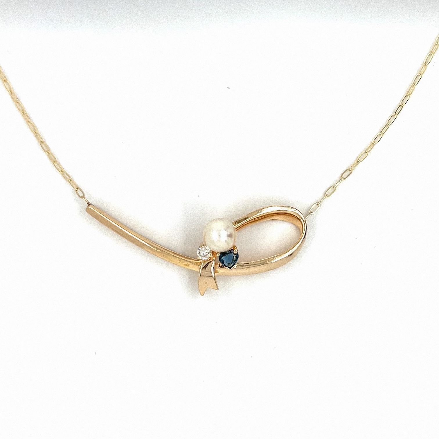 Gold necklace with a pearl, small blue stone, and diamond accents.