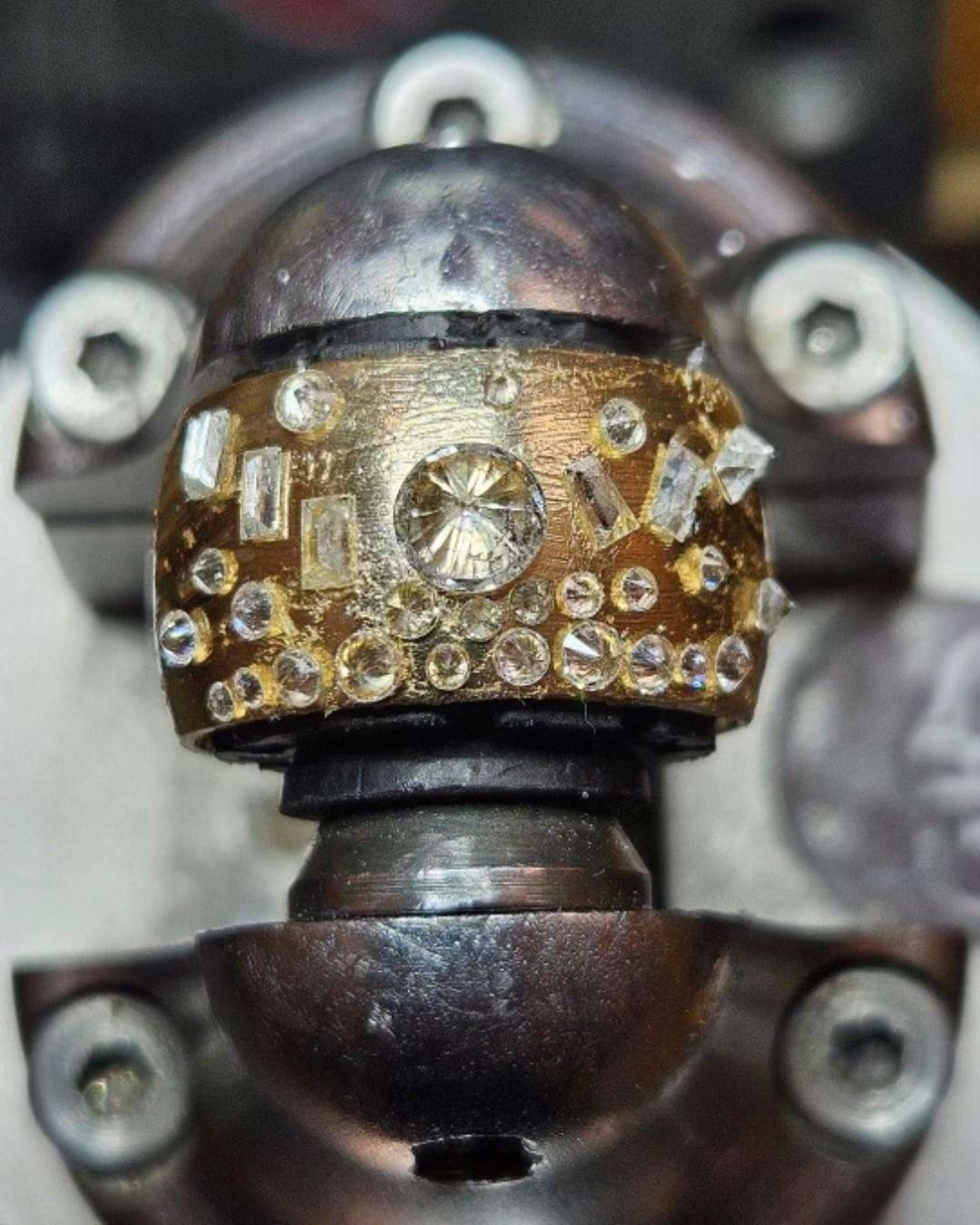 Jeweled metal object with many clear and gold accents, against blurred gray background.
