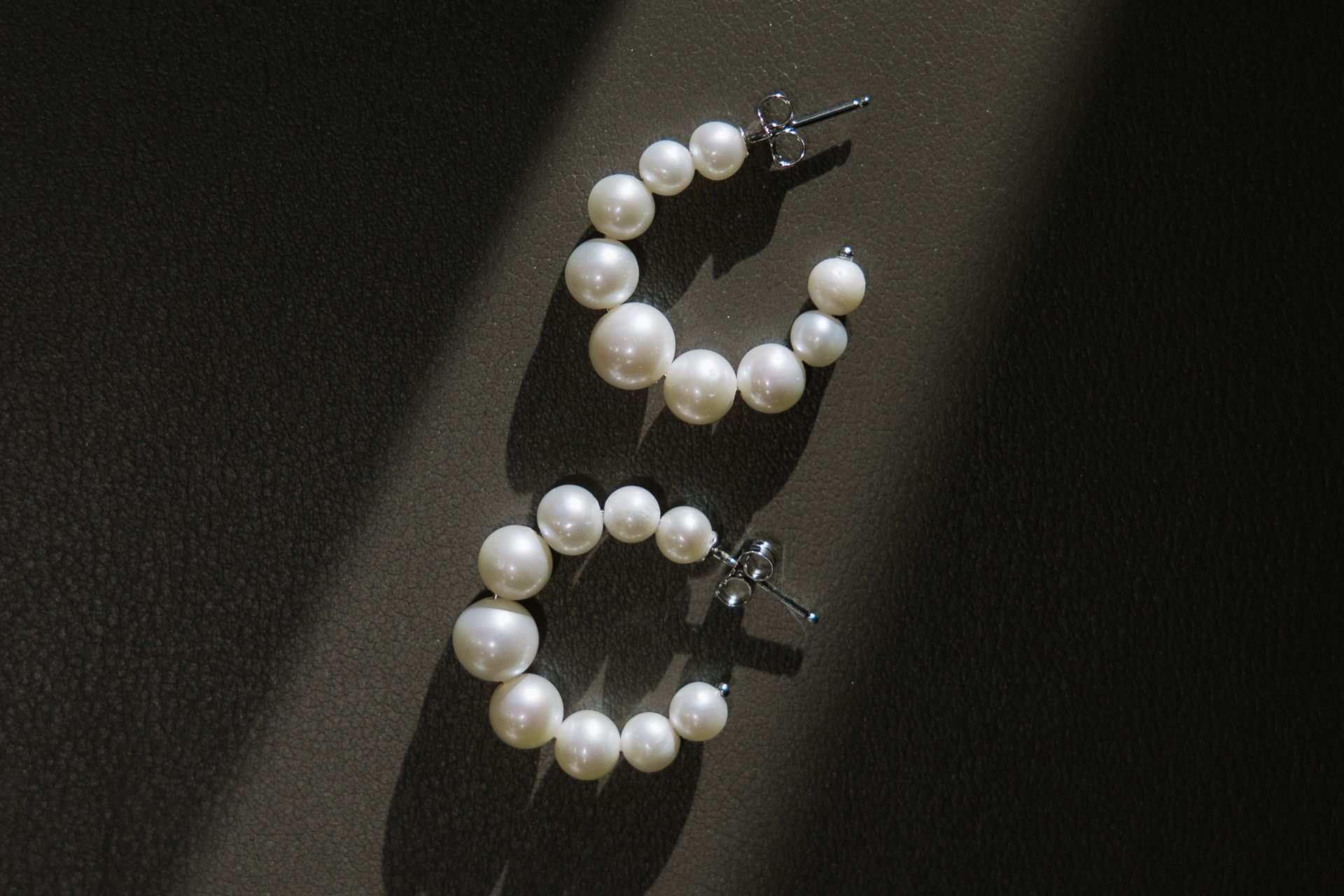 A pair of pearl hoop earrings are sitting on a black surface.