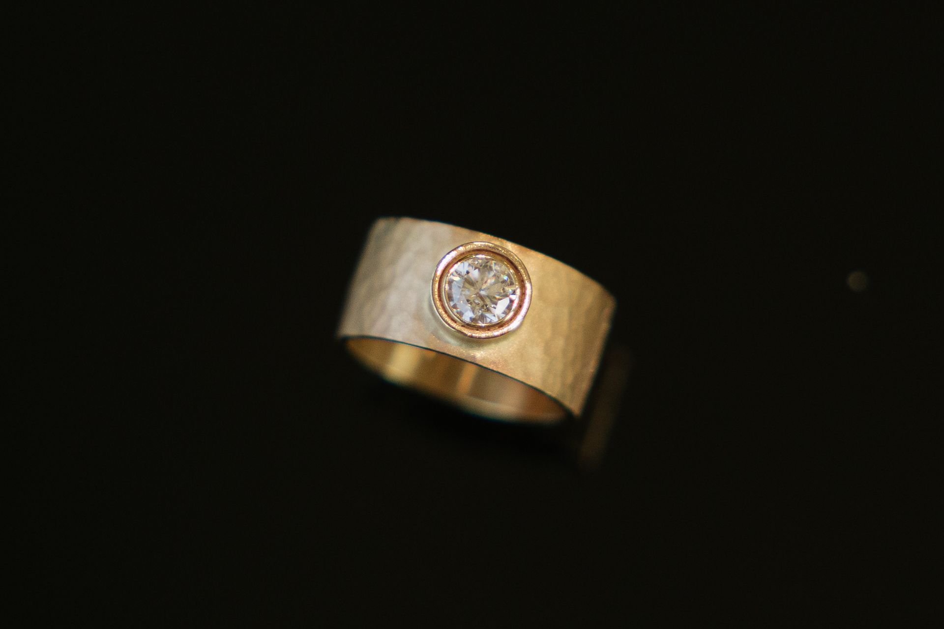 A gold ring with a diamond in the center on a black background.
