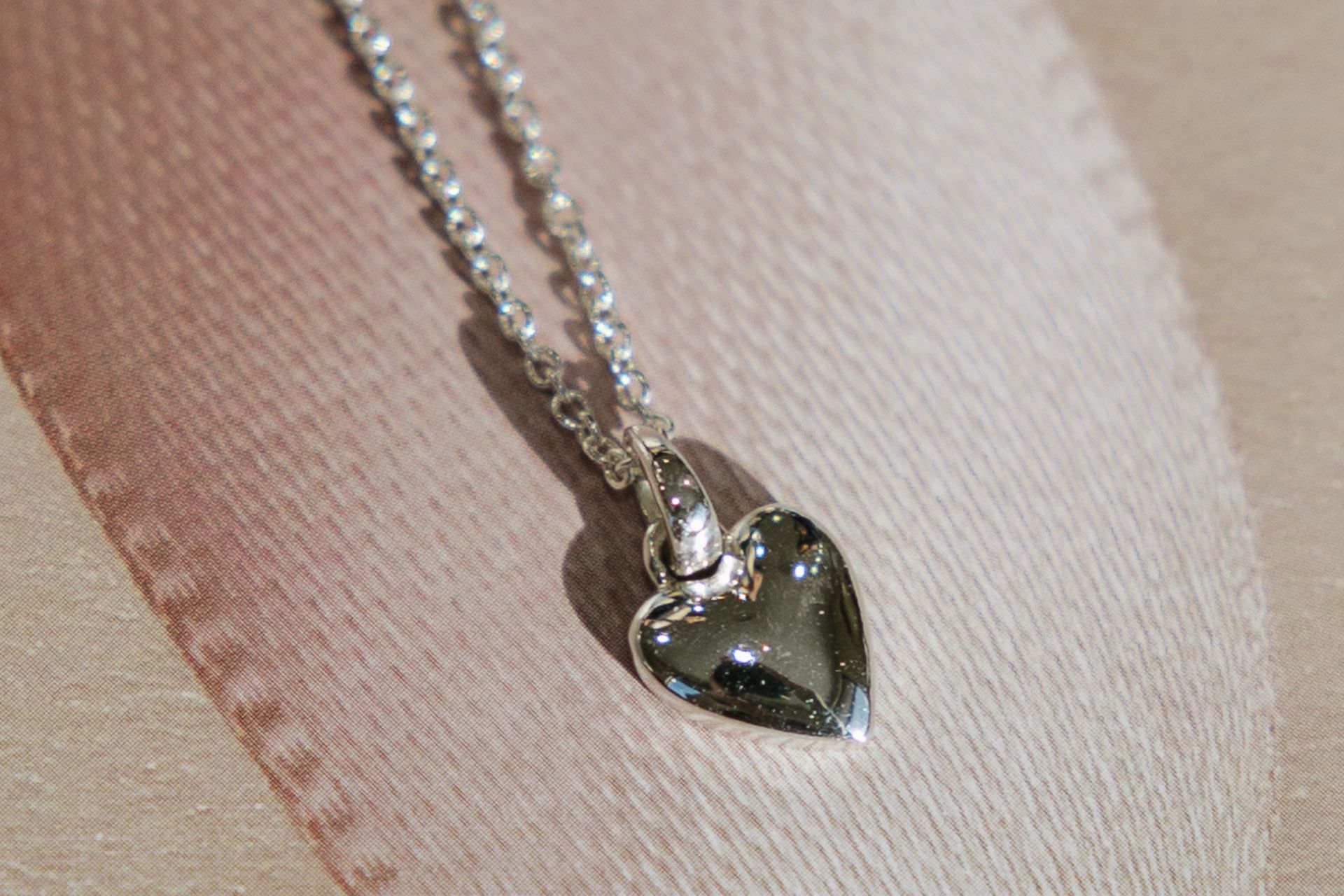 A close up of a necklace with a heart shaped pendant on a pink cloth.