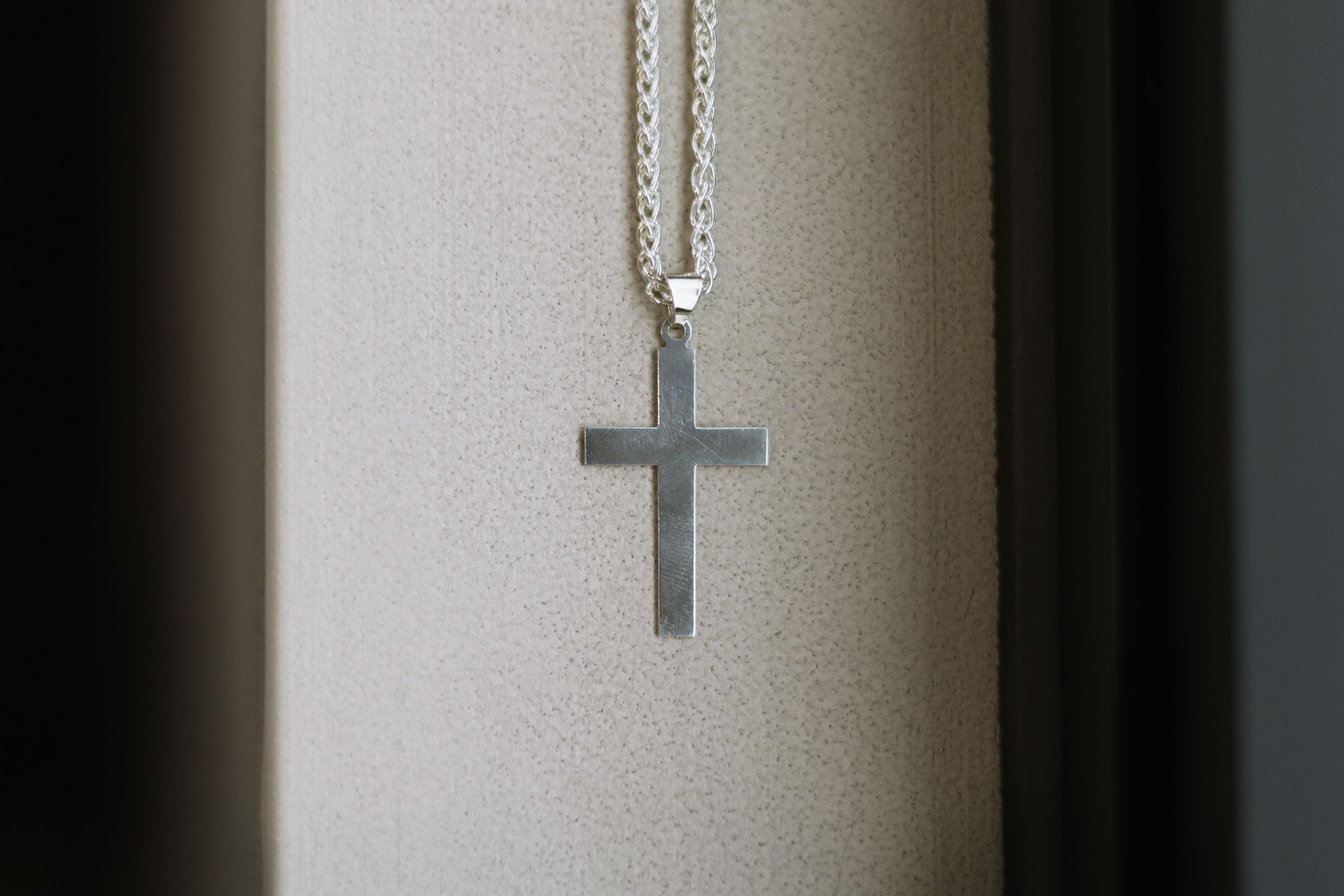 A silver cross necklace is hanging on a chain.