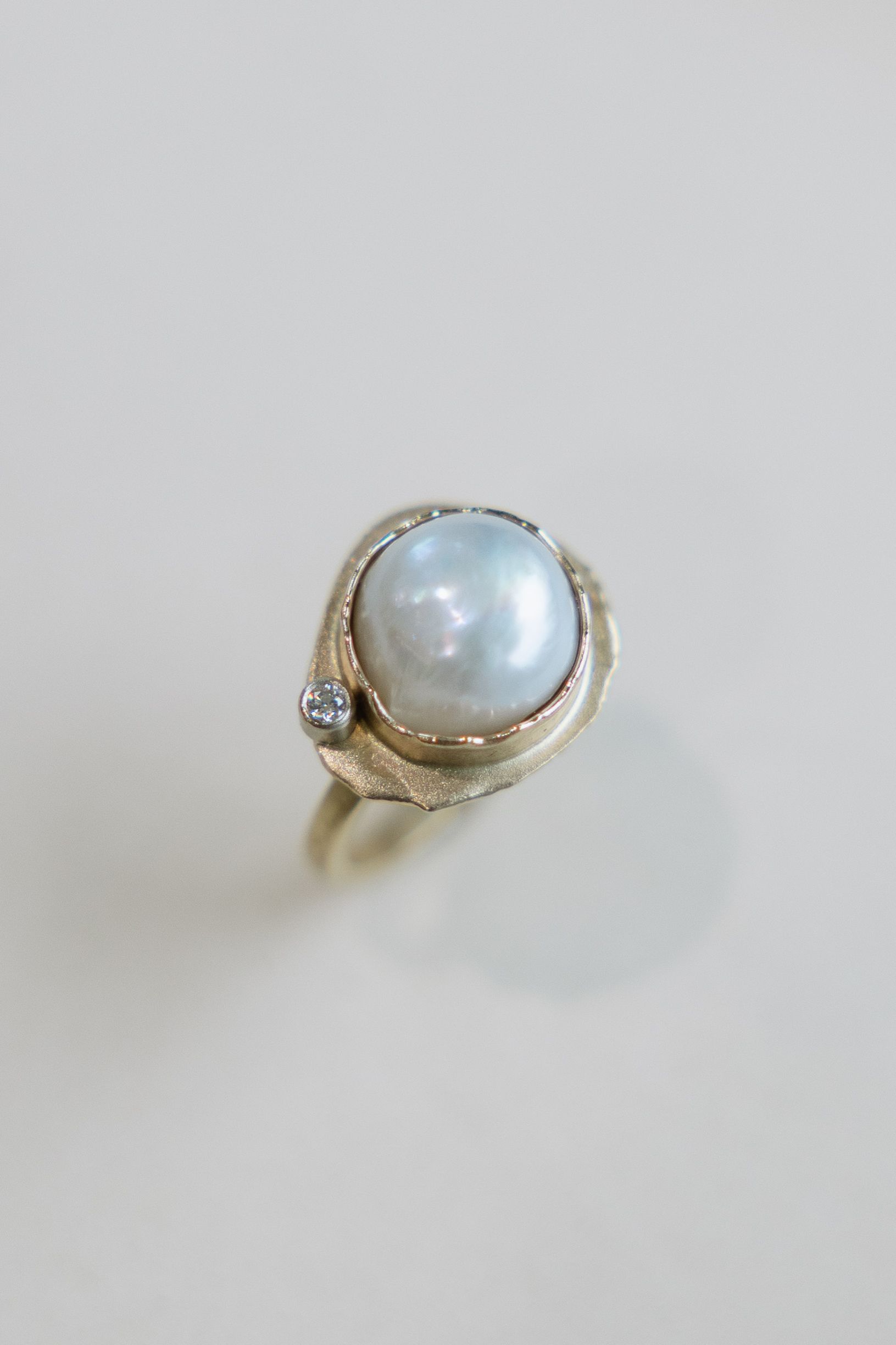 A gold ring with a pearl and a diamond on a white surface.