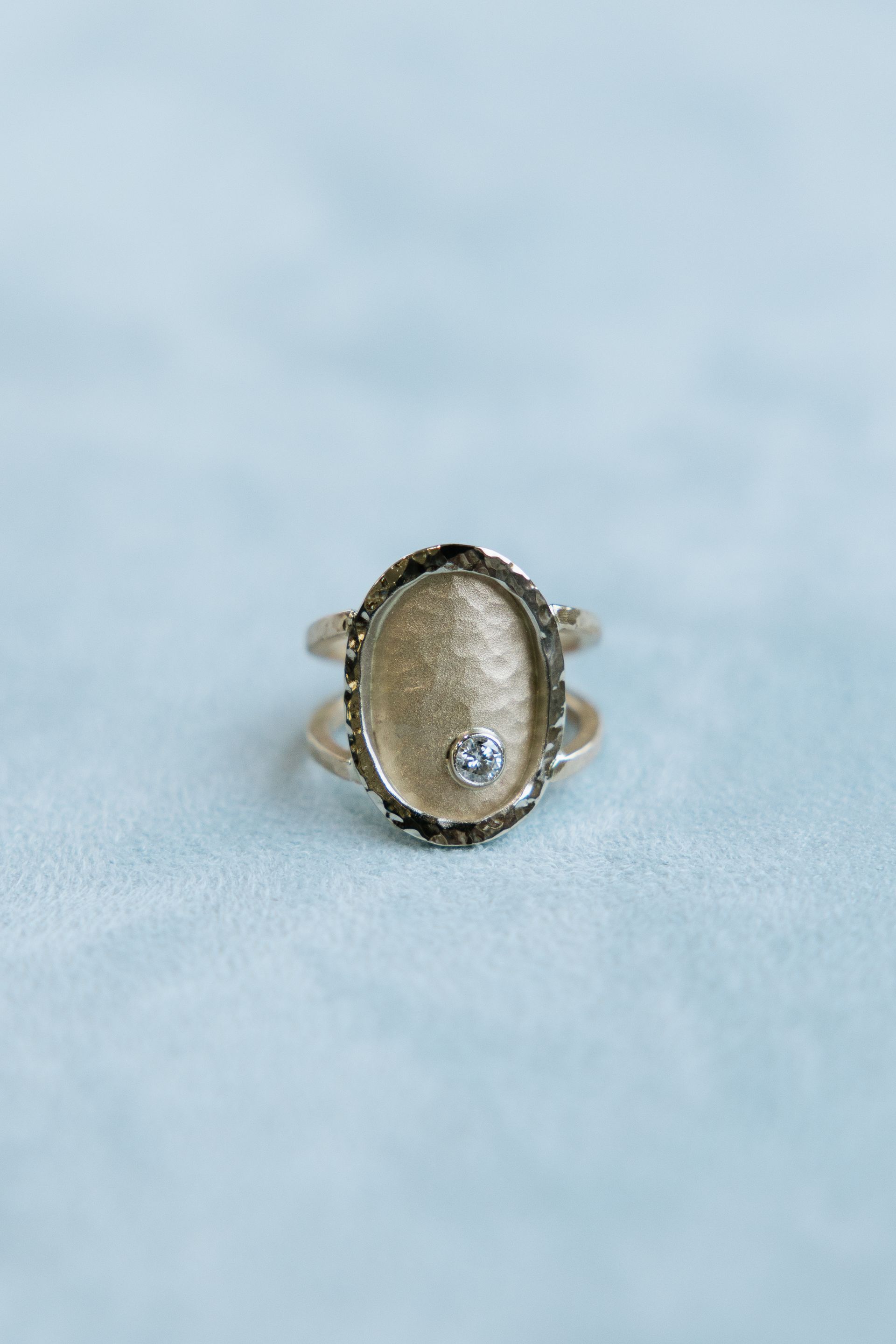 A gold ring with a diamond in the center is sitting on a blue surface.