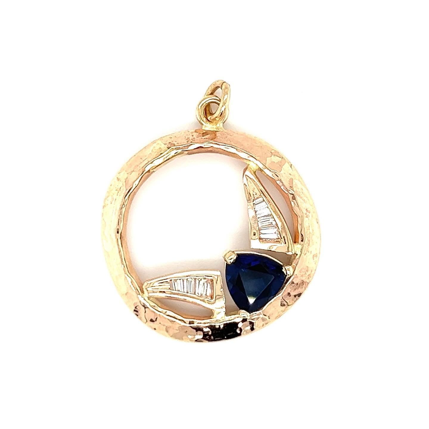 Gold pendant with a circular frame and sailboat design, featuring blue and white gems.