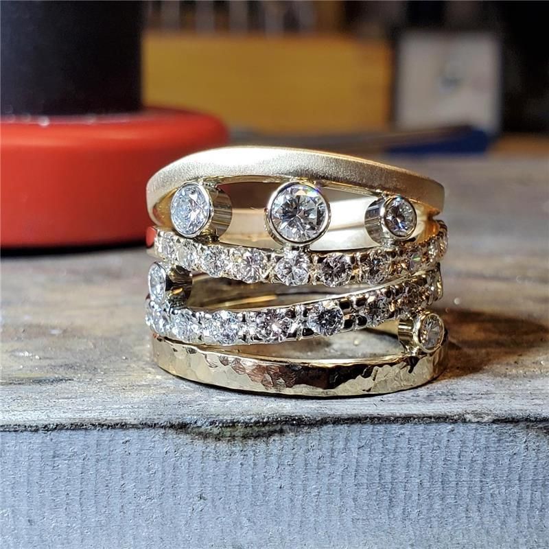 Close-up of gold rings with diamonds, stacked on a workbench.