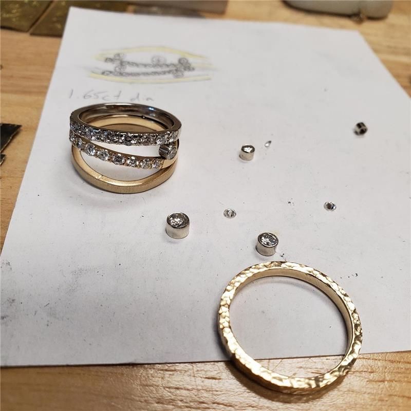 Jewelry rings and loose diamonds on a workbench, with sketches in the background.