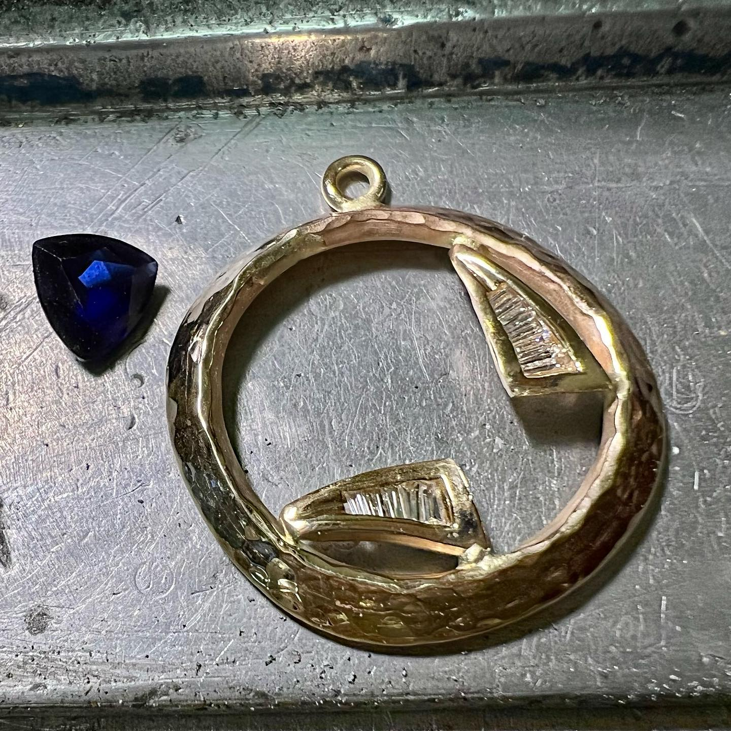 Blue gemstone next to a gold pendant with two sections of baguette diamonds.