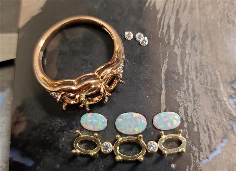 Gold ring with diamonds and opals, along with loose opals and diamonds on a dark surface.