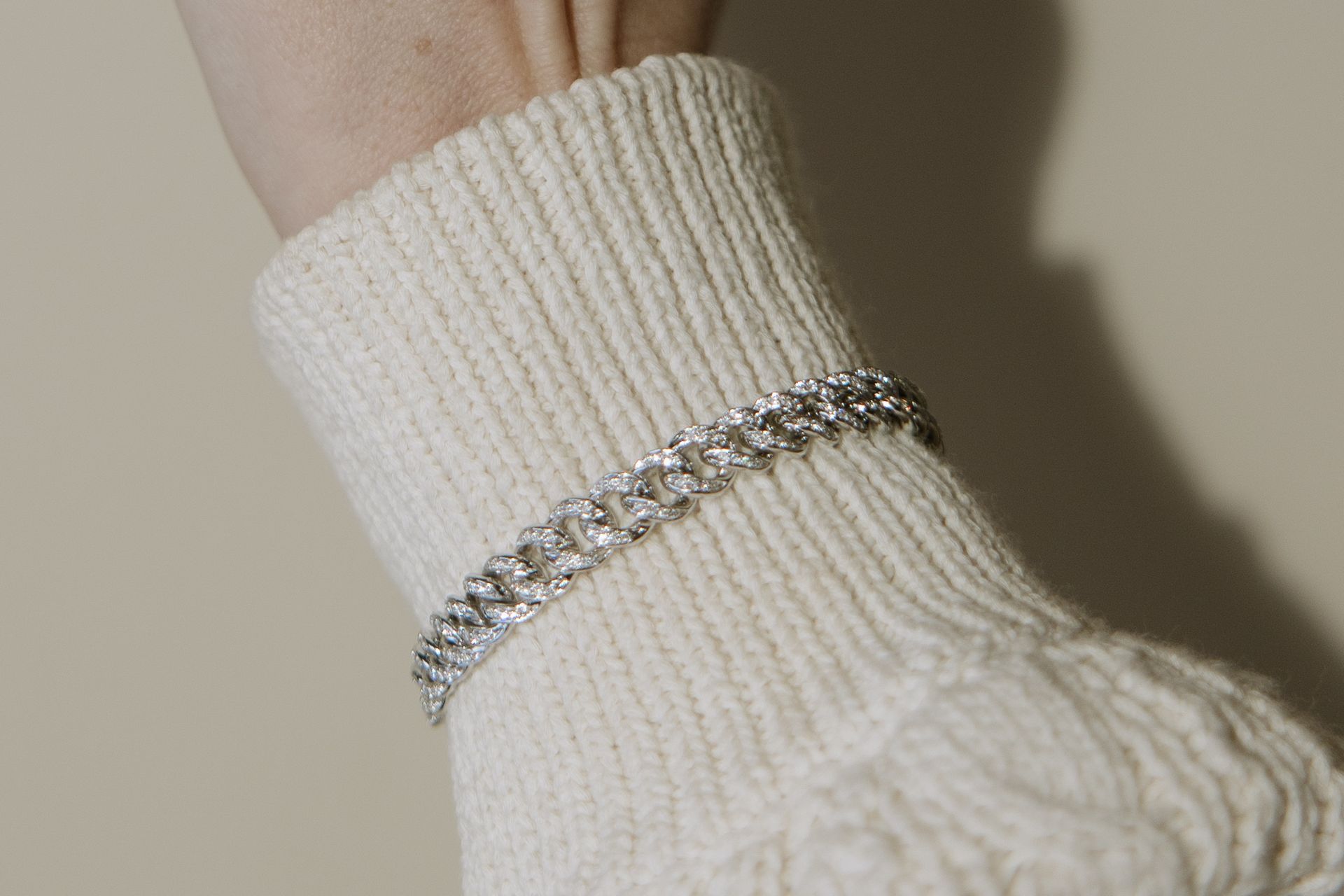 Silver bracelet on a person's wrist, over a white knit sweater sleeve.