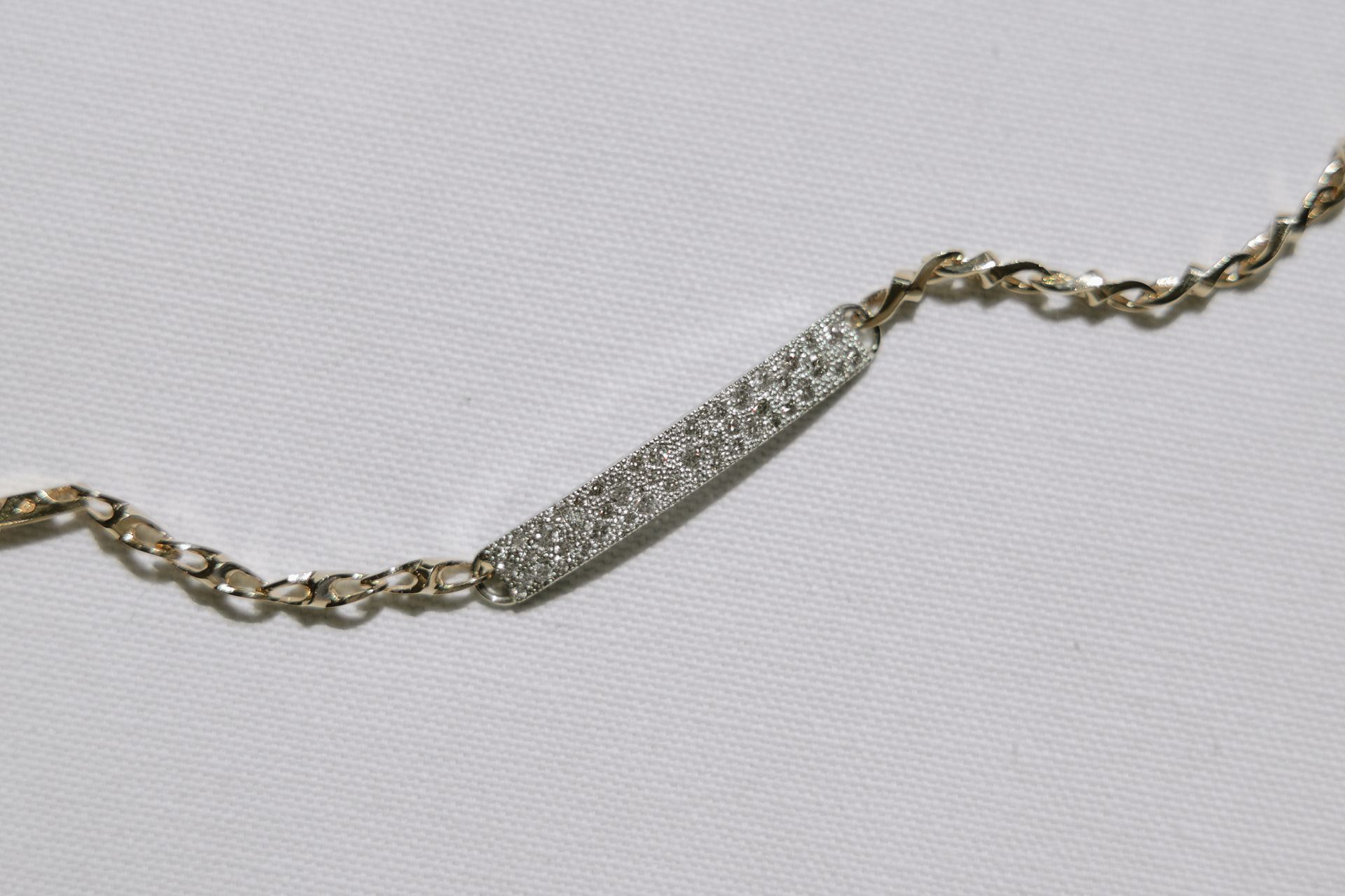 Diamond-studded bar pendant on a delicate gold chain, against a white background.