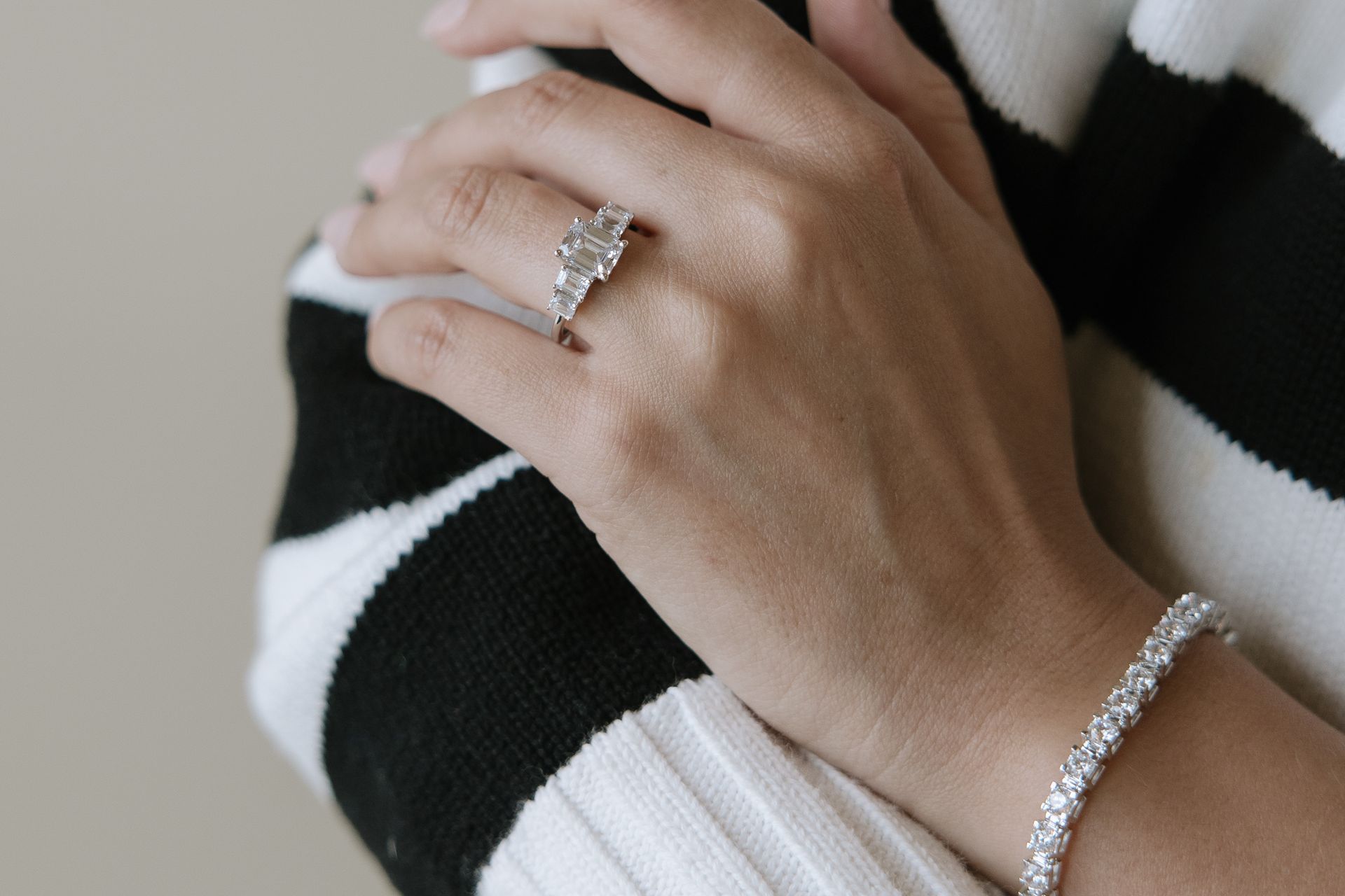Woman's hand with a diamond ring and bracelet, resting on a black and white striped sleeve.