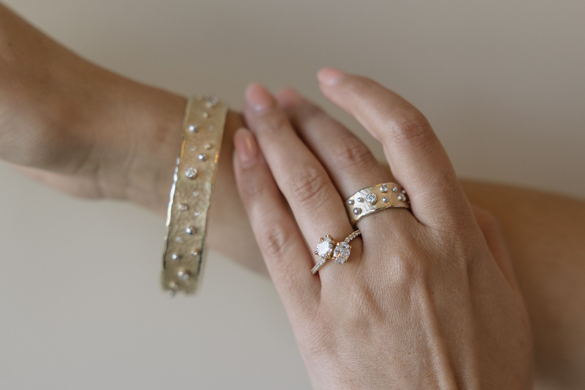 Woman's hand and wrist adorned with a silver bracelet and two rings, all with small, scattered gemstones.