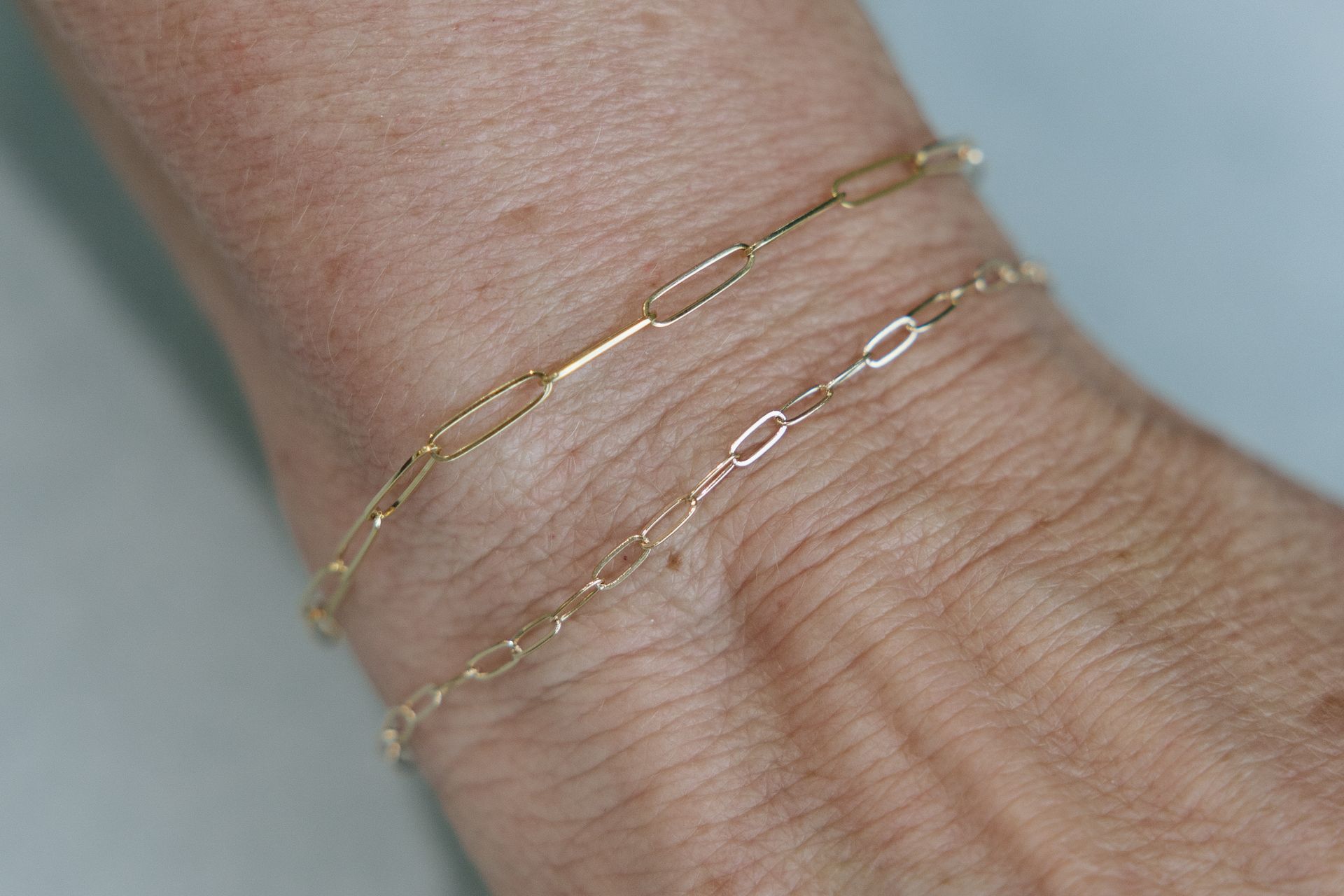 Two delicate gold chain bracelets on a person's wrist.