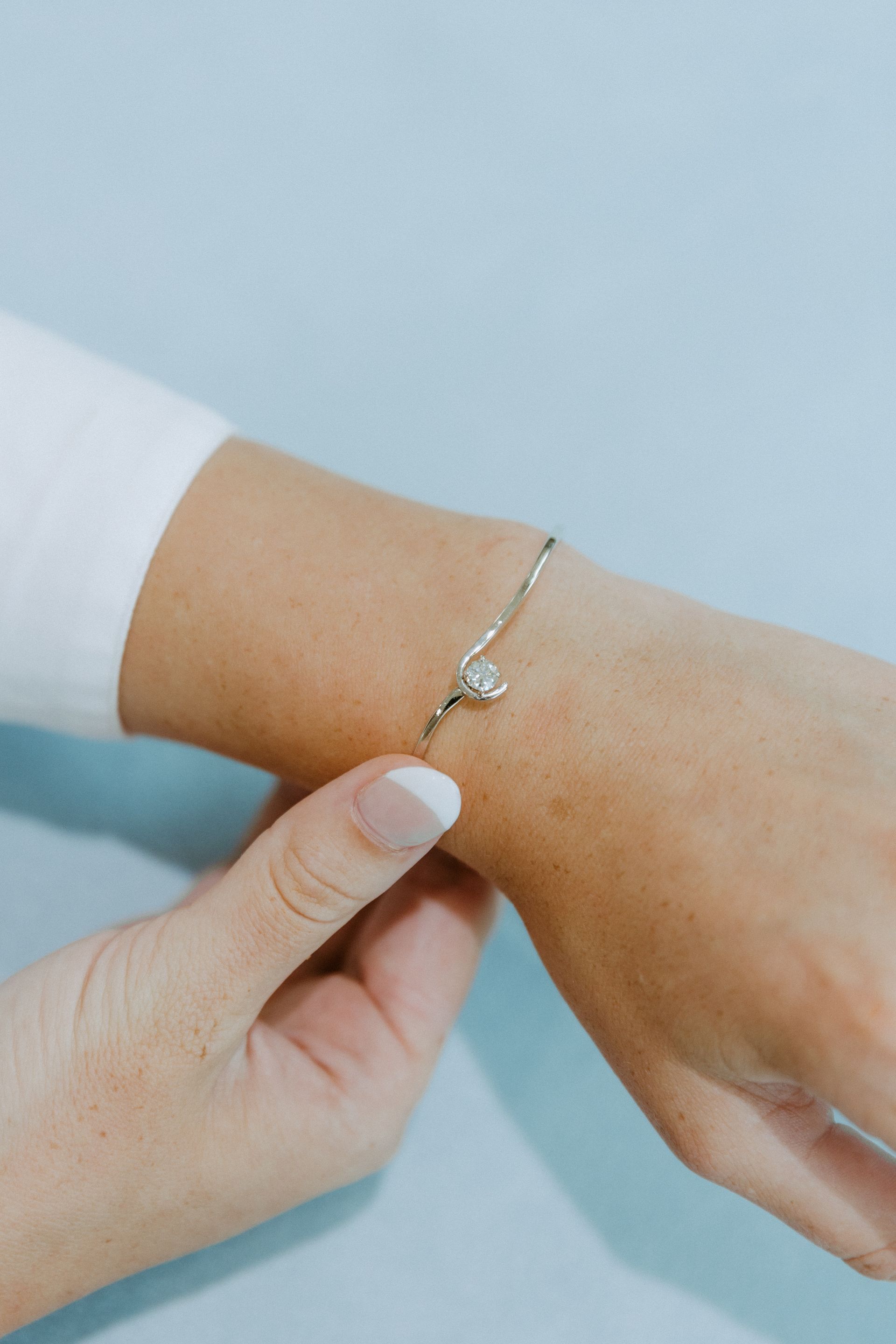 Woman's hand wearing a silver bracelet with a small, sparkly charm, against a light blue backdrop.