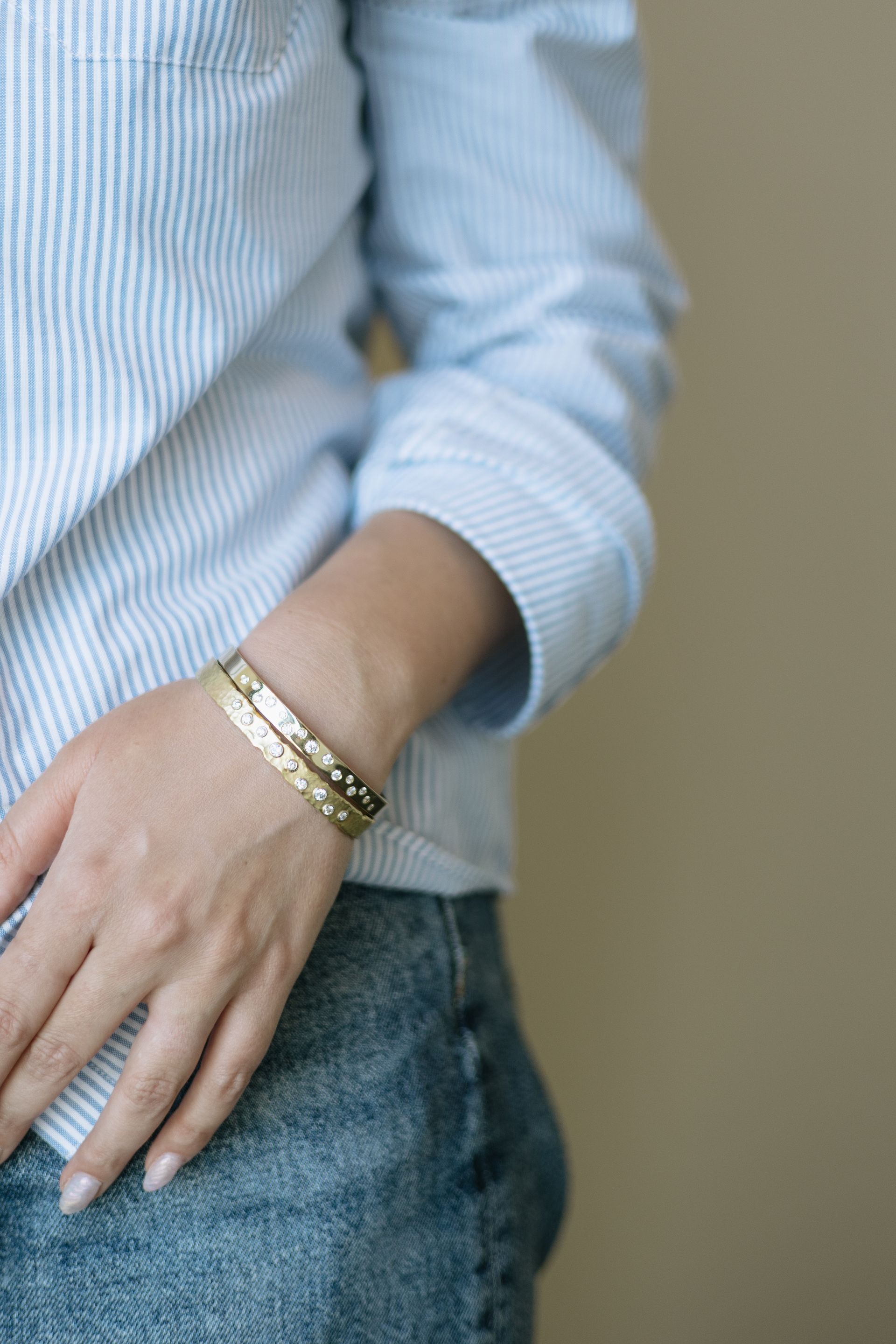 Woman wearing gold bracelets, light blue striped shirt, and denim jeans.