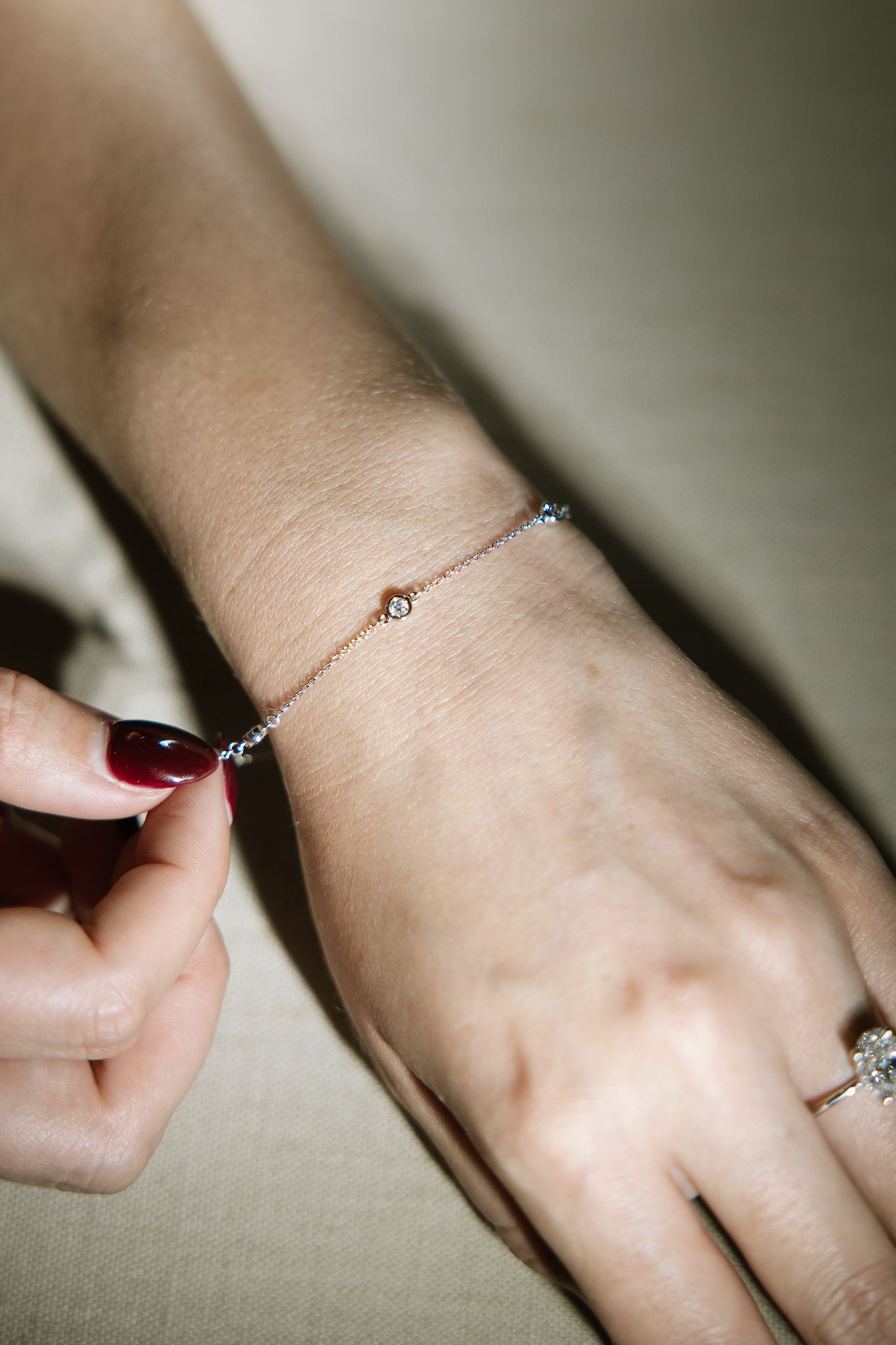 A hand wearing a thin bracelet and a ring with a diamond, adjusting the clasp.
