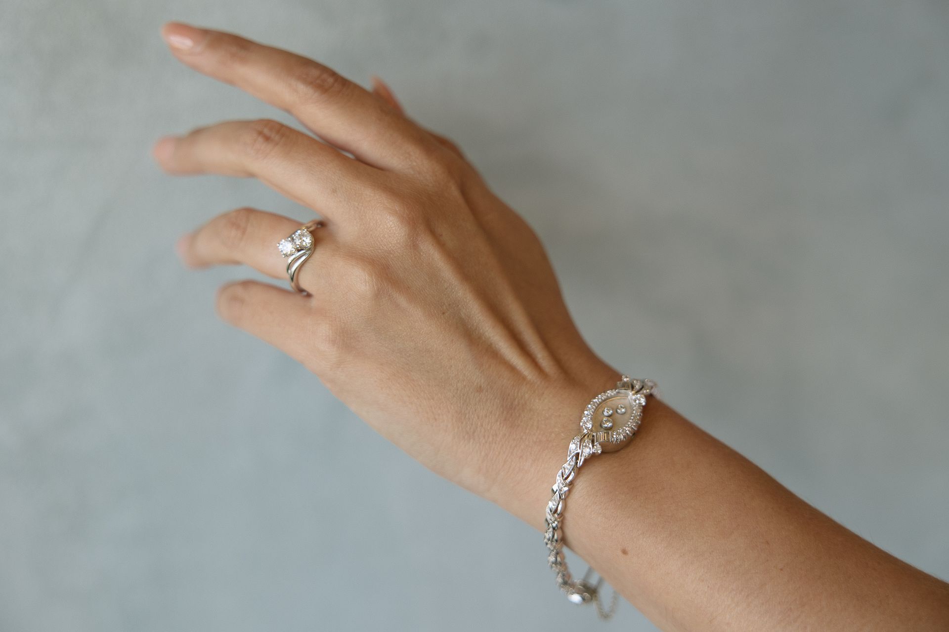 Hand with diamond ring and silver bracelet, extended against a light blue wall.