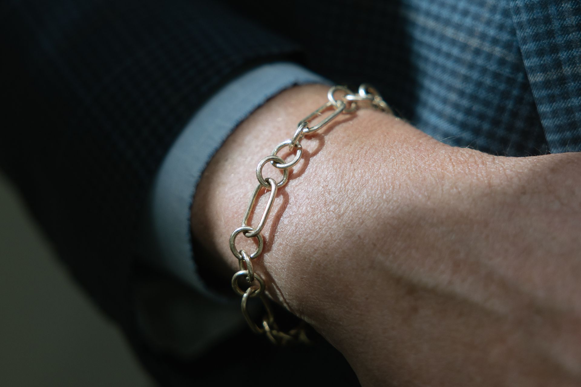 Gold link bracelet on a wrist, worn with a suit.
