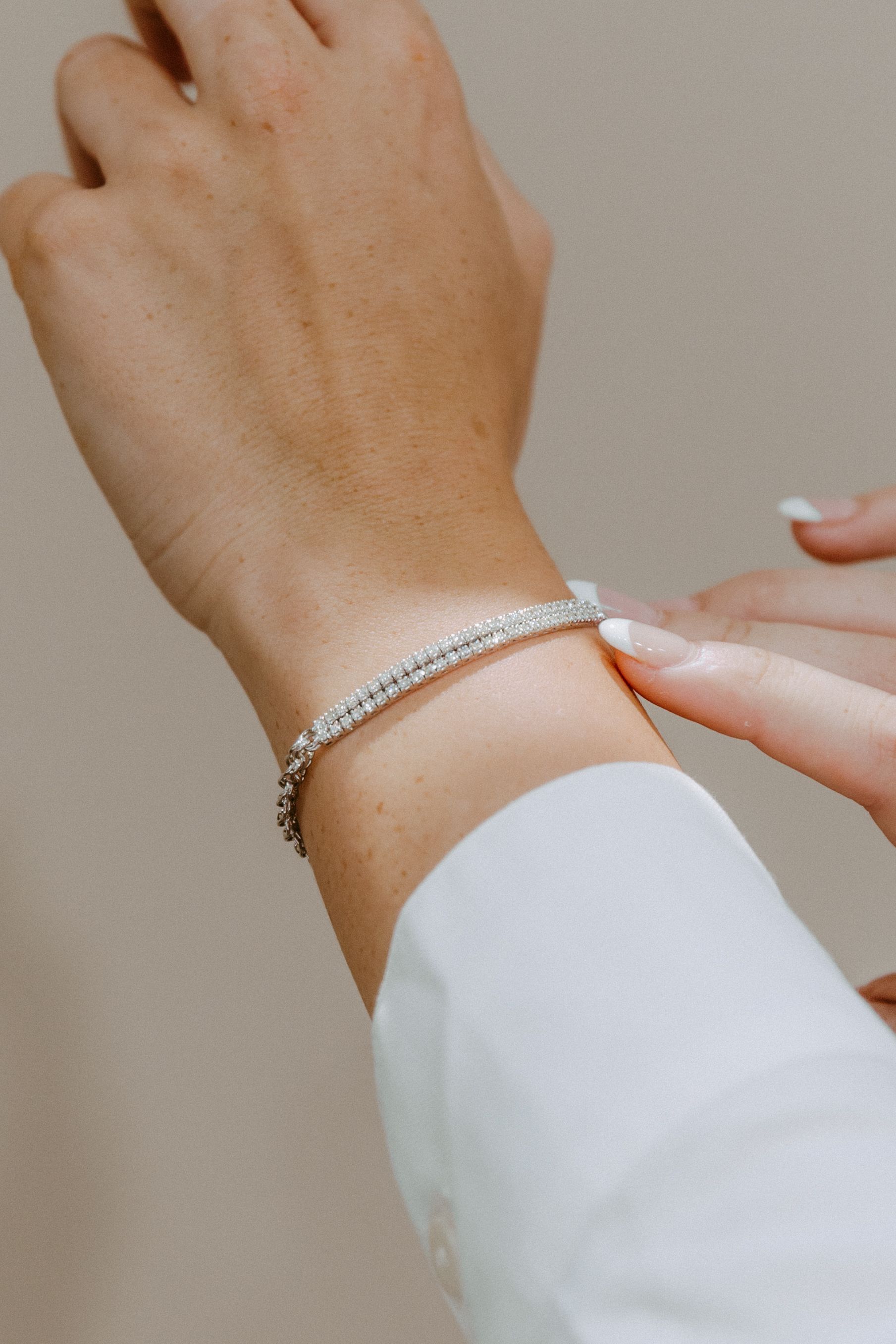 Person's hand adjusting a diamond tennis bracelet on wrist, wearing a white shirt.