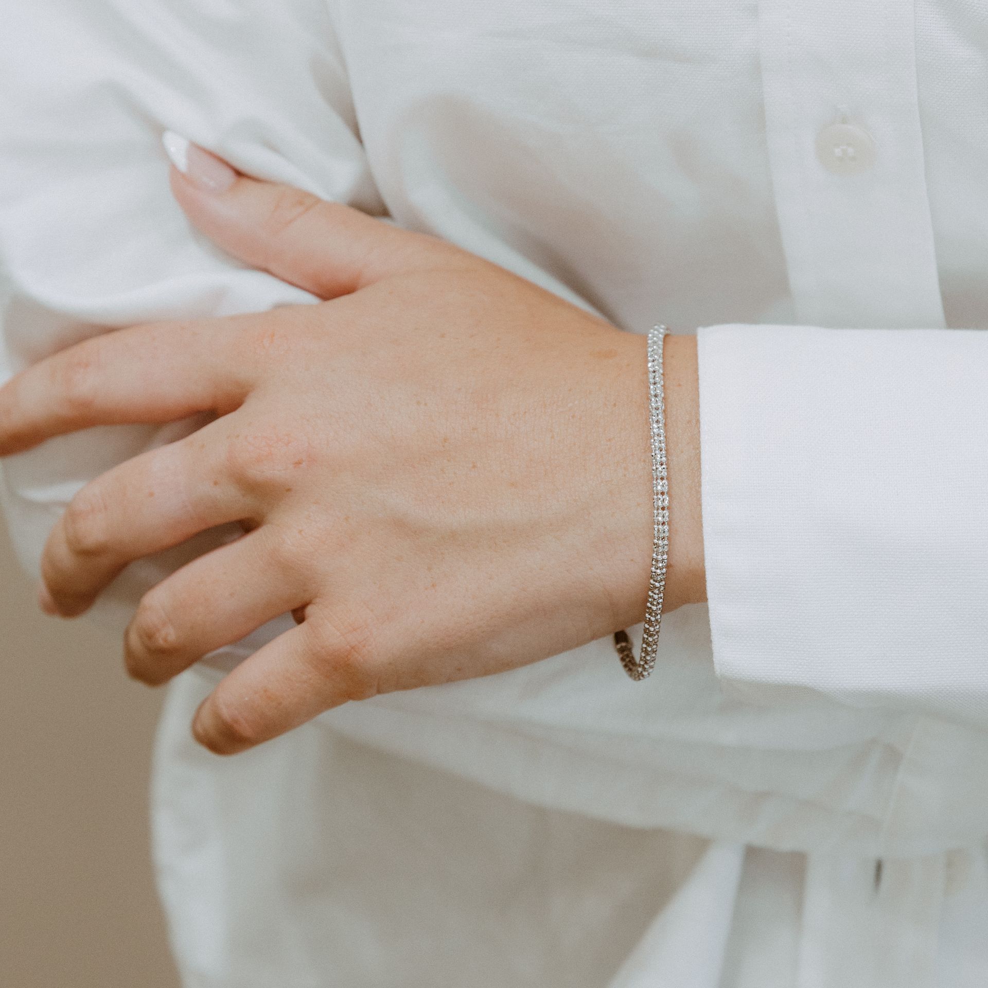 Hand wearing a diamond tennis bracelet, resting on a white shirt.