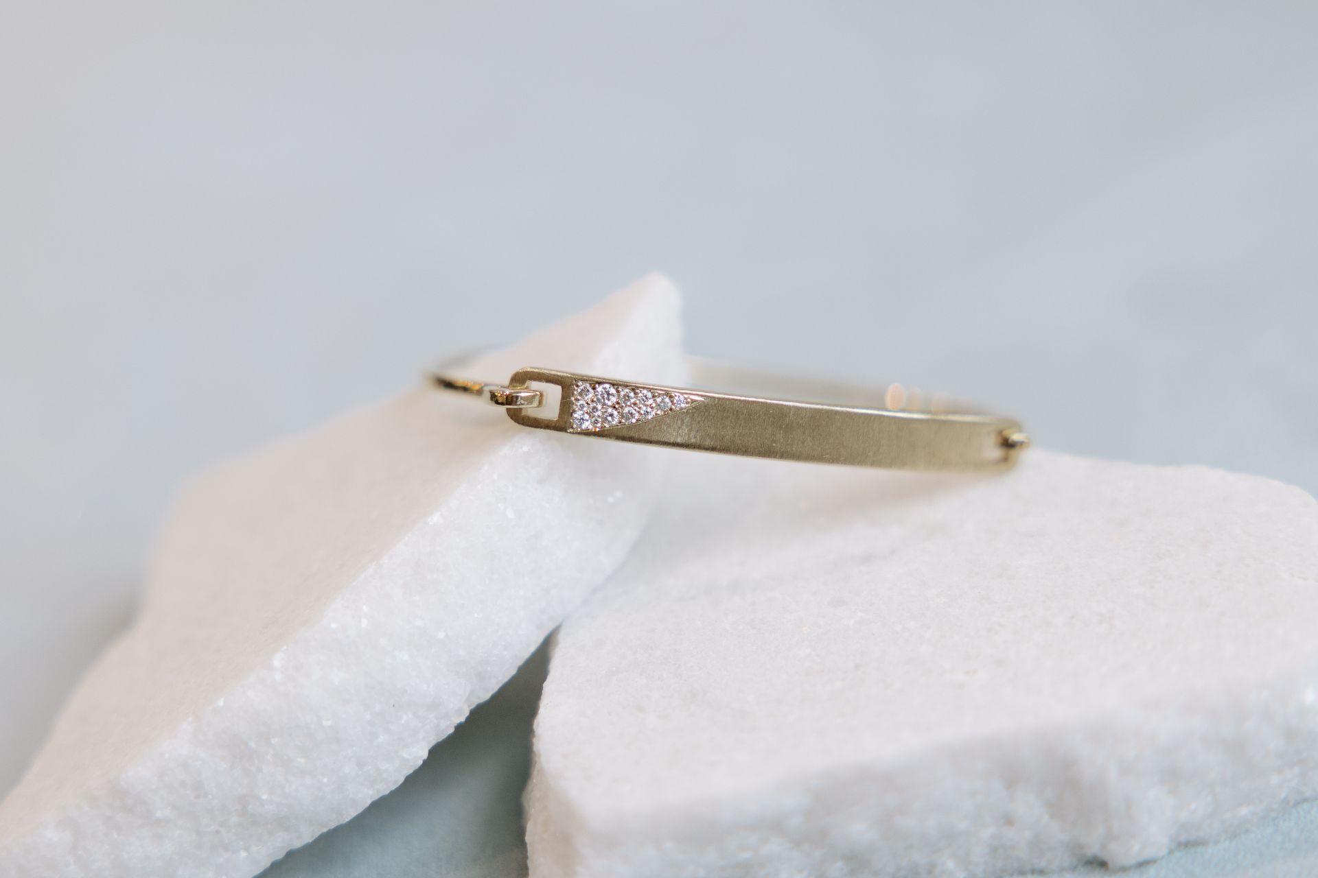 Gold bracelet with a triangle of small gems on a white stone against a pale blue background.