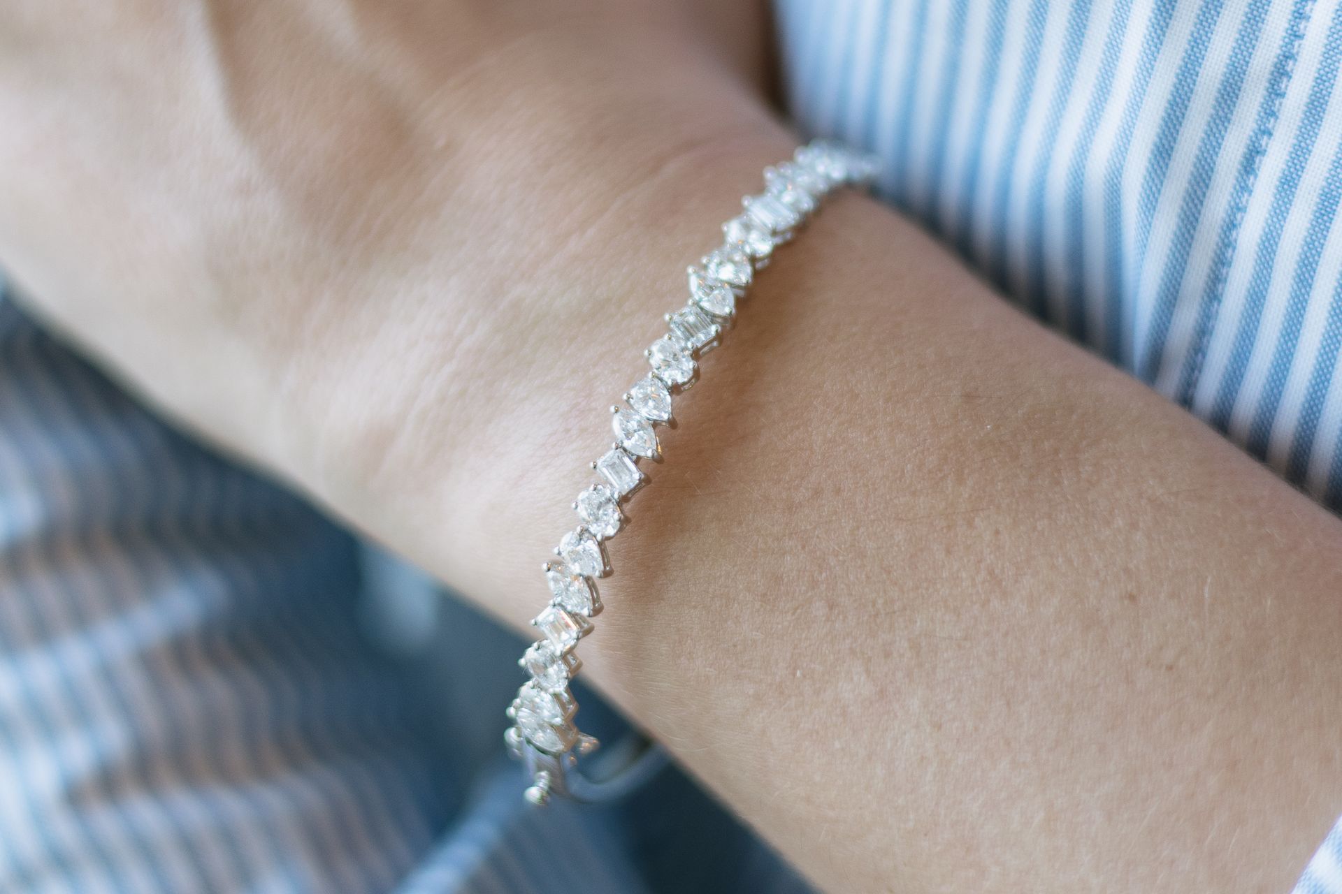 Silver bracelet with many small, sparkling stones on a person's wrist, against a blue and white striped shirt.