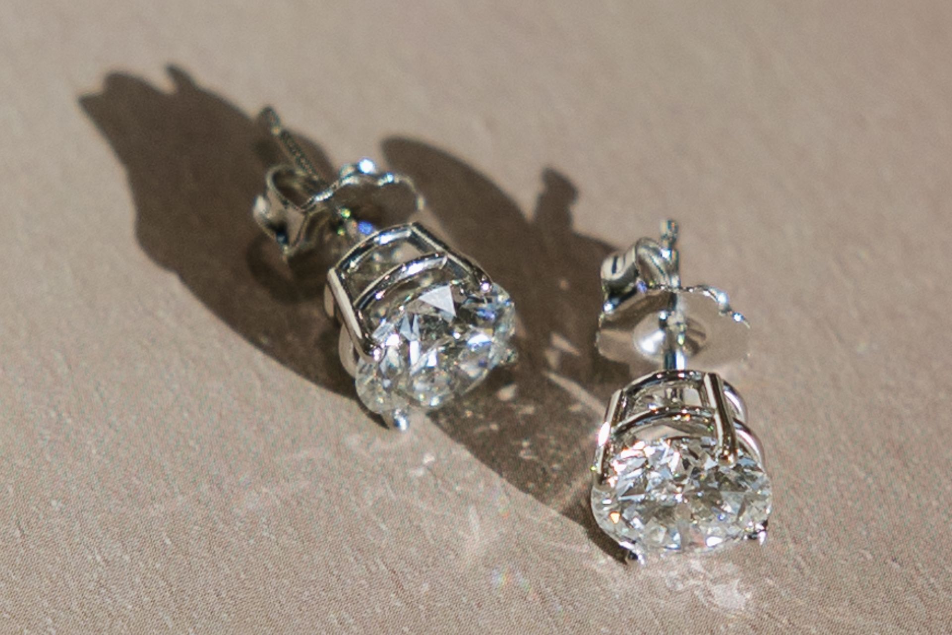 Pair of diamond stud earrings on a beige surface.