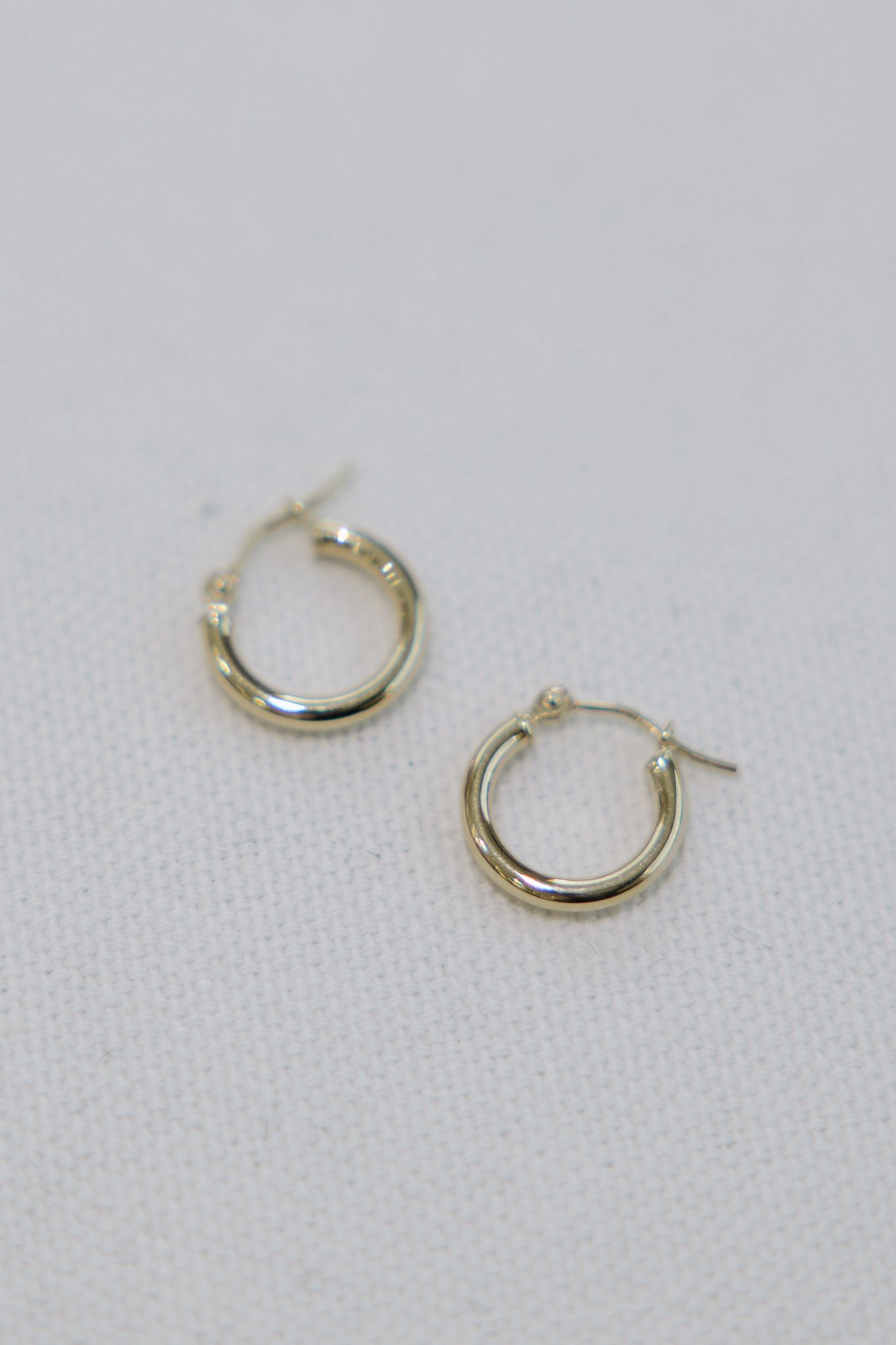 Two small, silver-colored hoop earrings on a white surface.