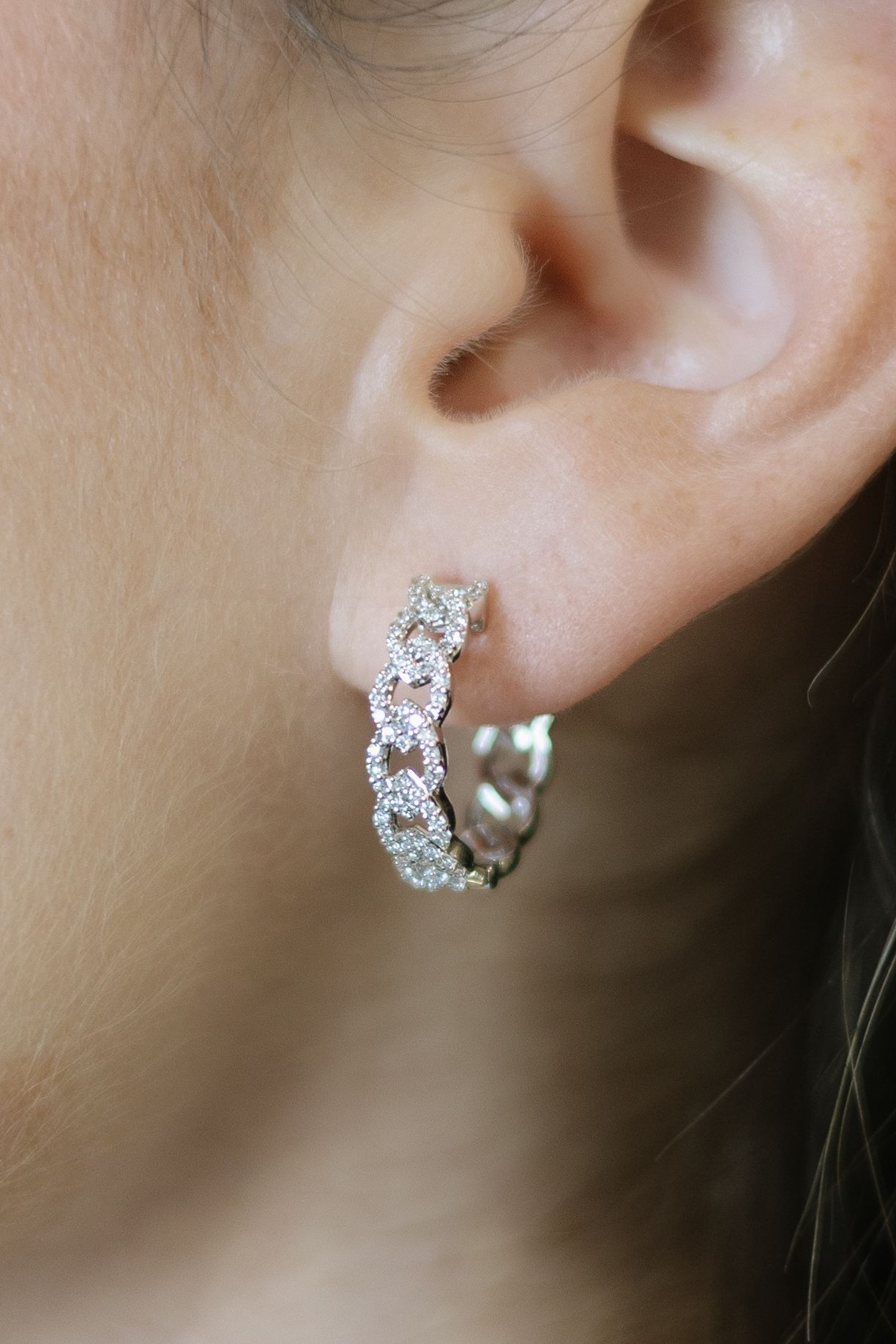 Silver hoop earring with sparkling stones on ear.