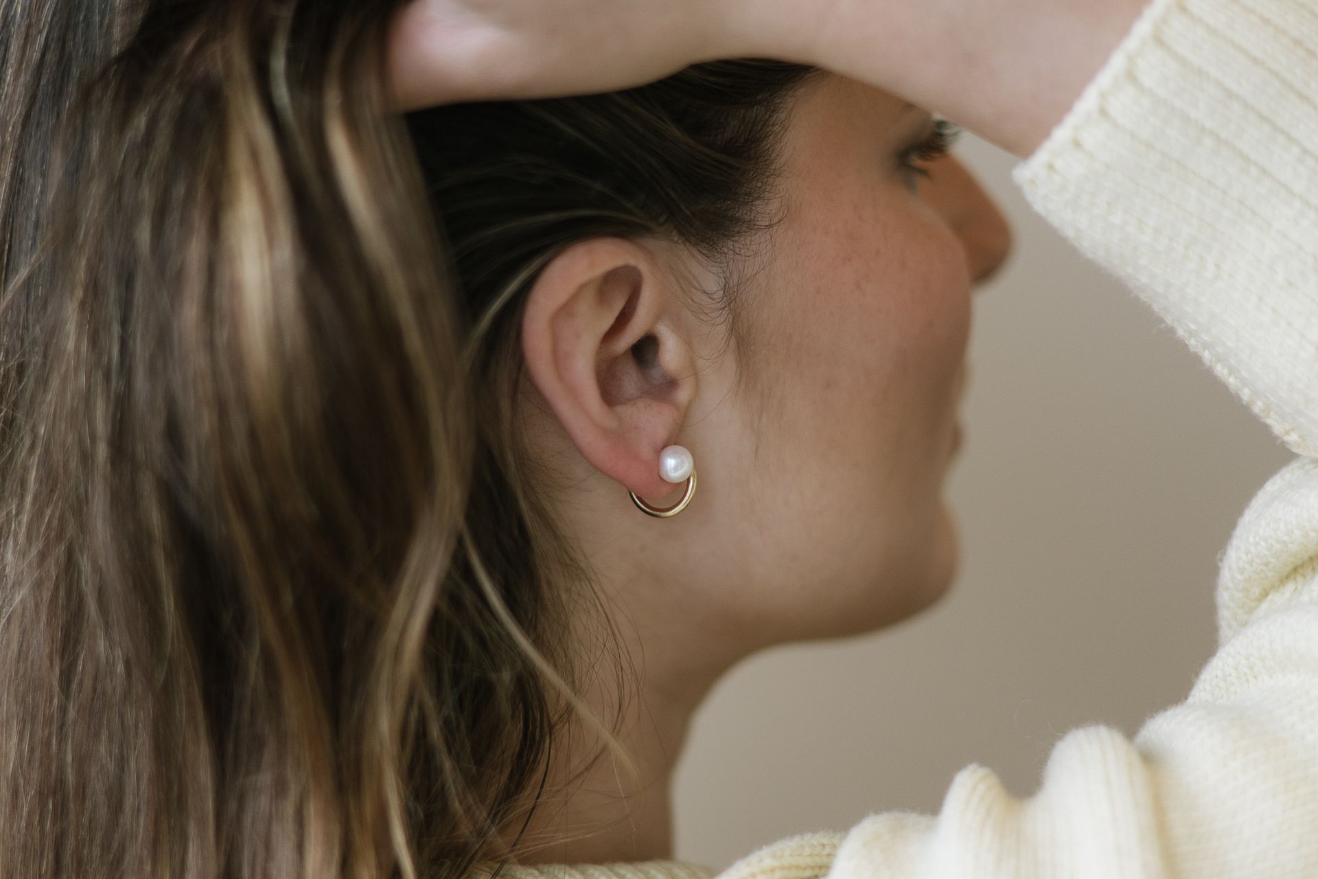 Woman with long hair wearing pearl earrings, hand in hair.