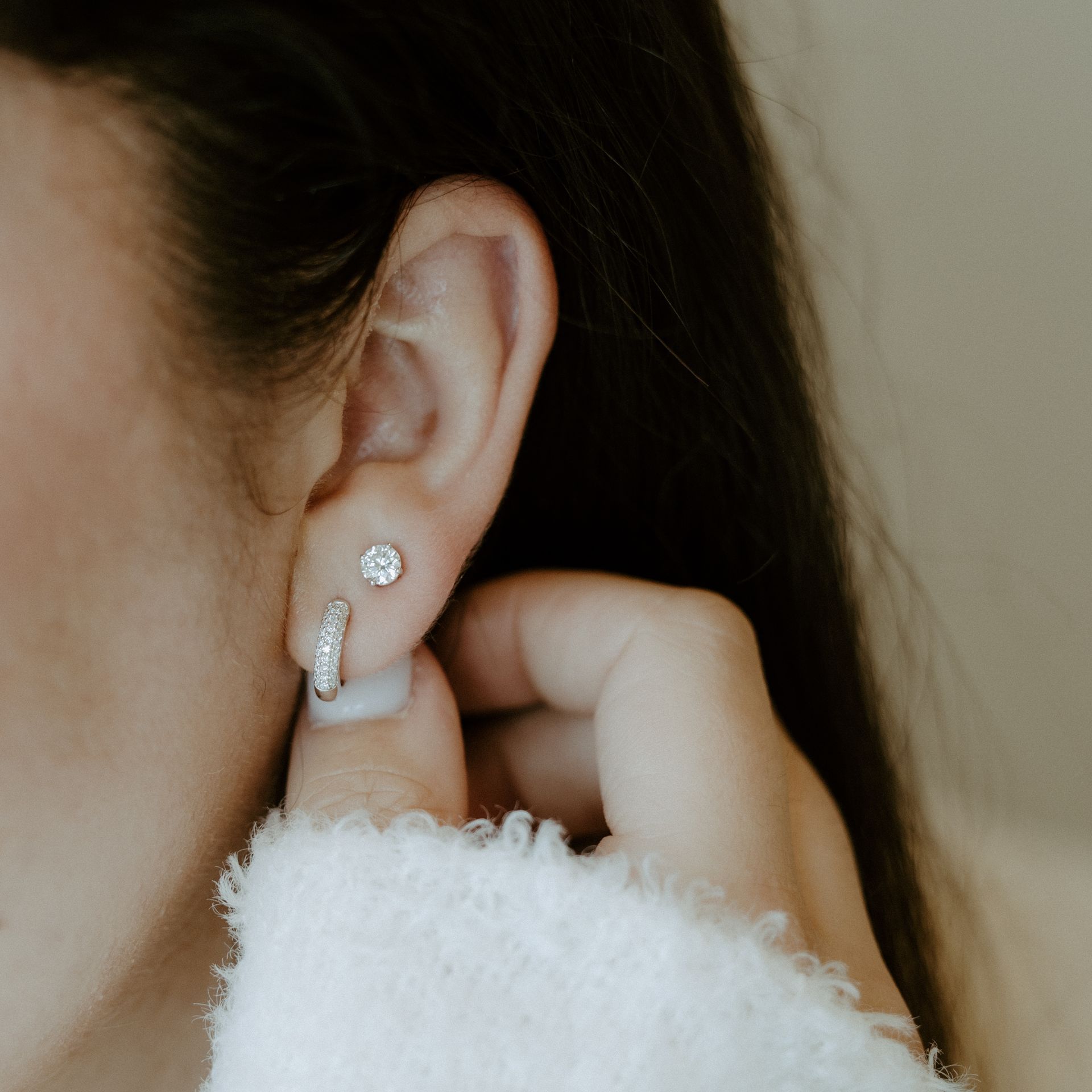 Close-up of ear with two silver earrings. Hand touches the earring on the lower lobe.