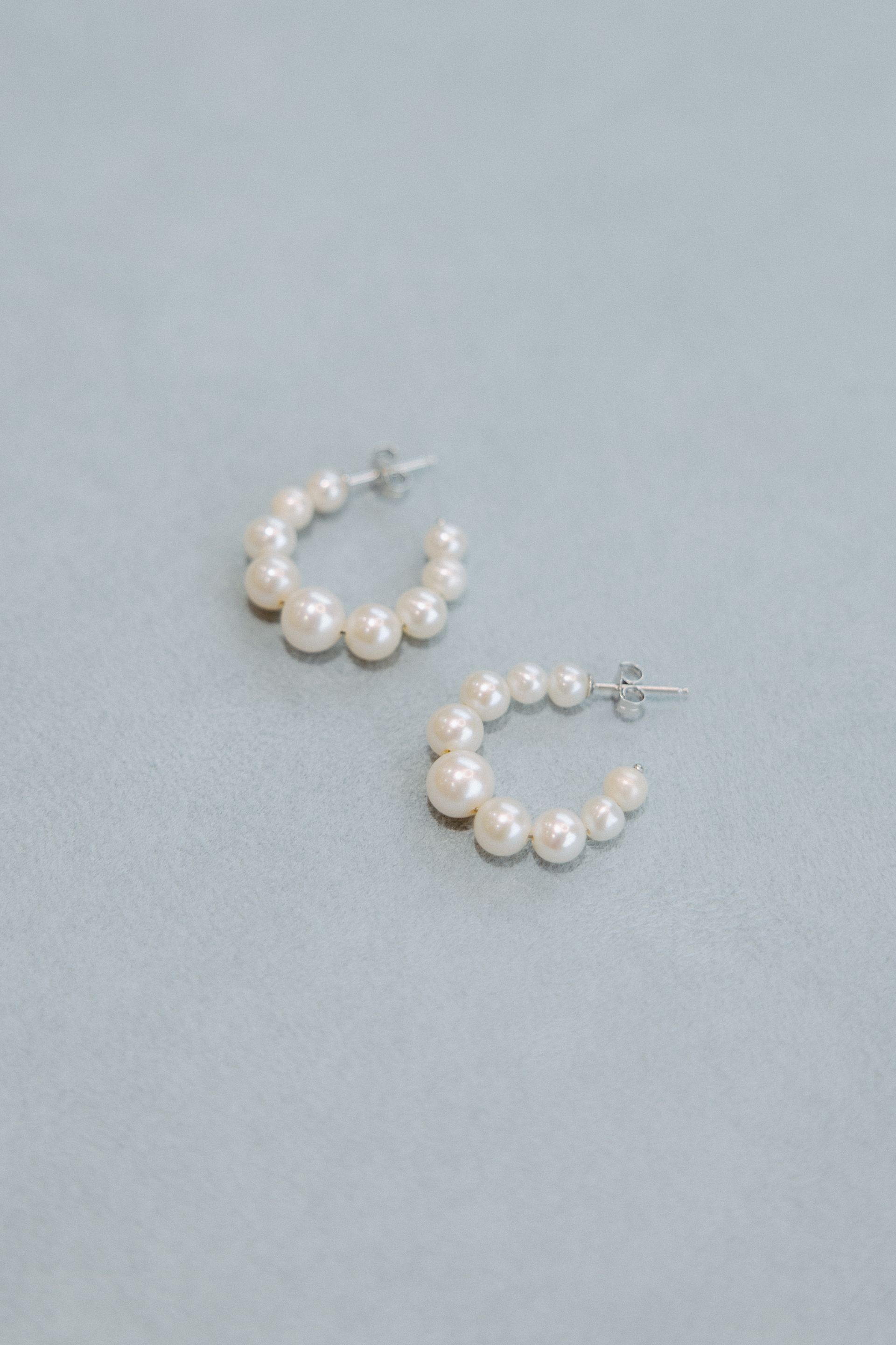 Pearl hoop earrings on a light blue fabric background.