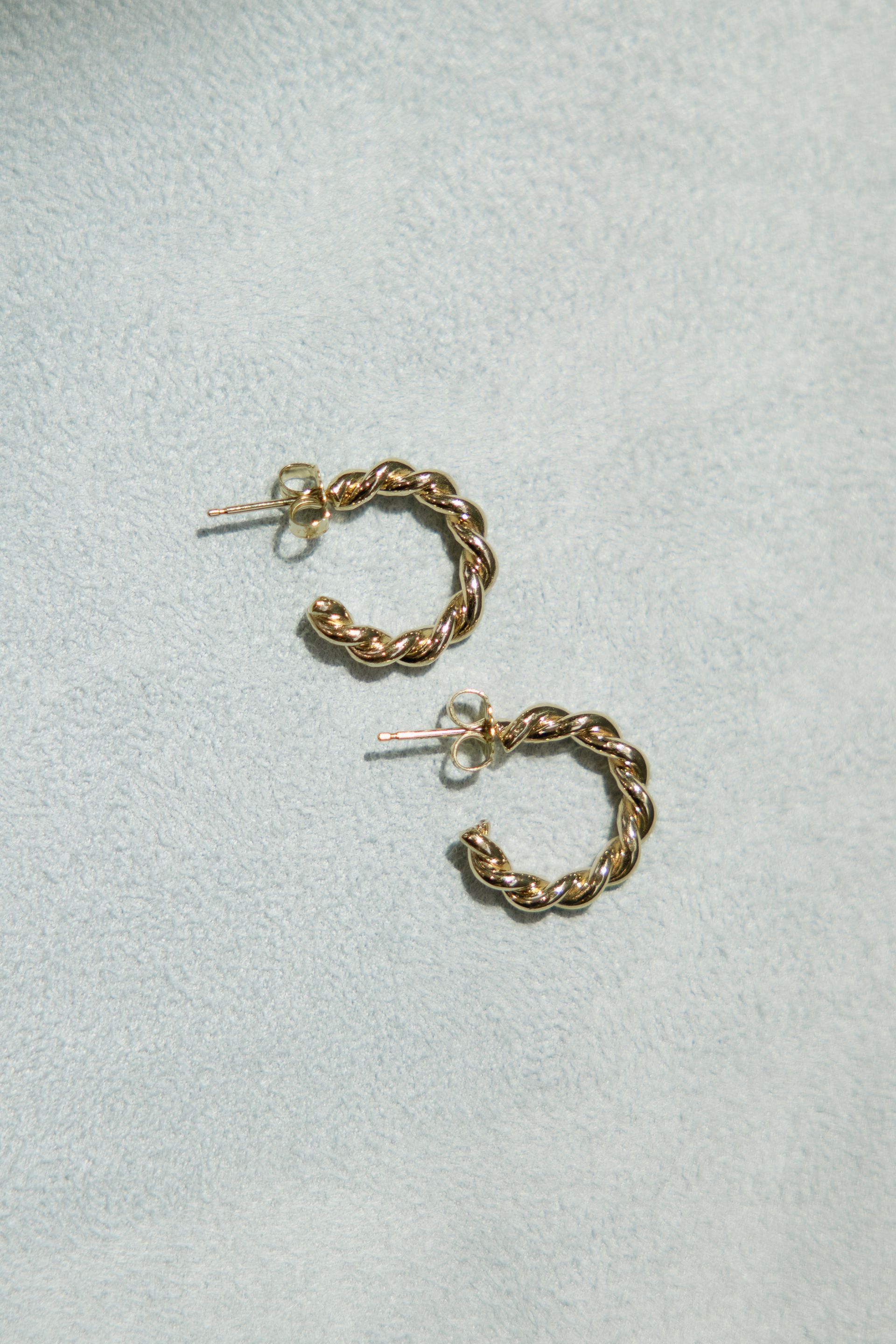 Gold hoop earrings with textured beaded design, set on a light blue surface.