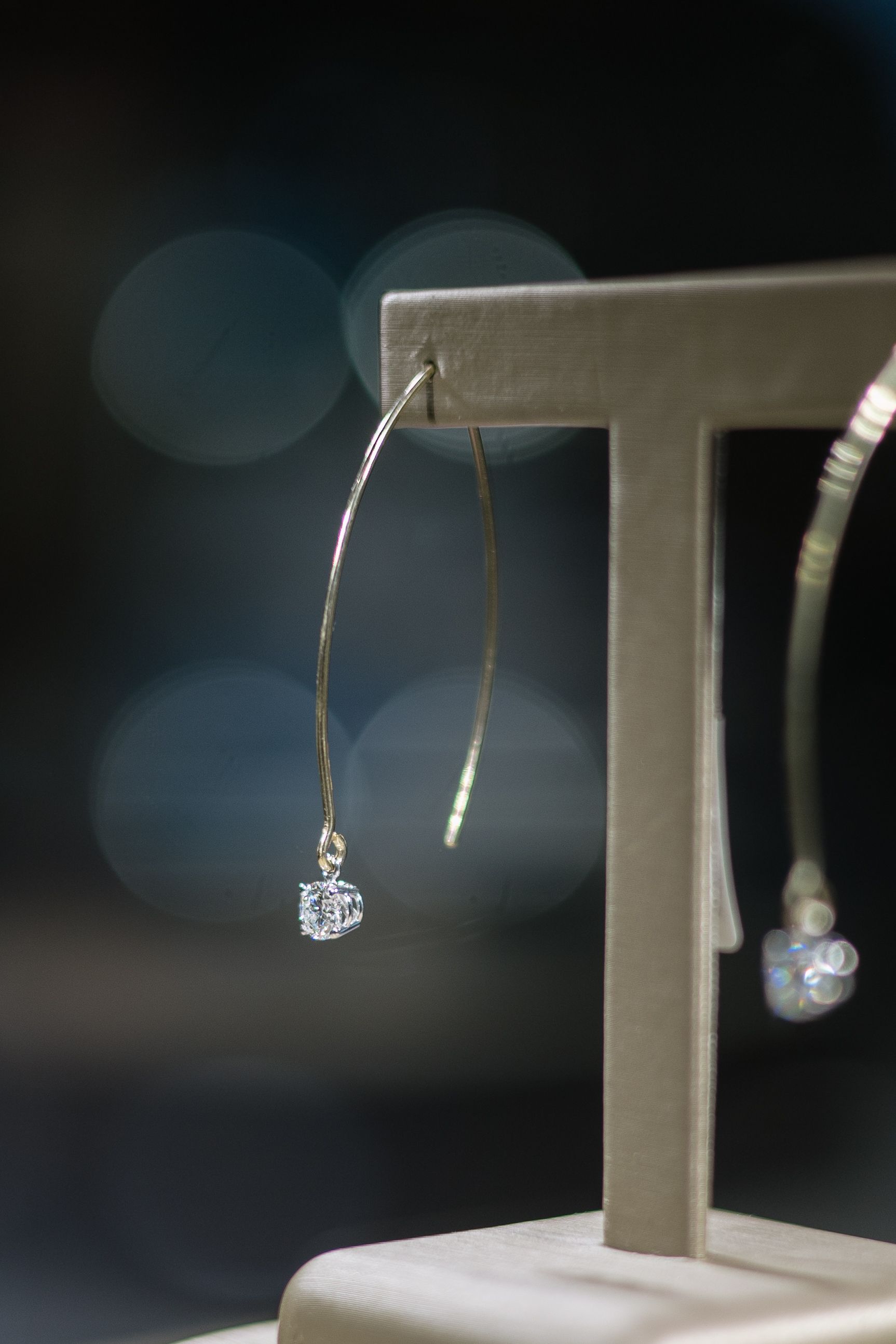 Gold hoop earring with a small, clear gemstone, displayed on a jewelry stand.